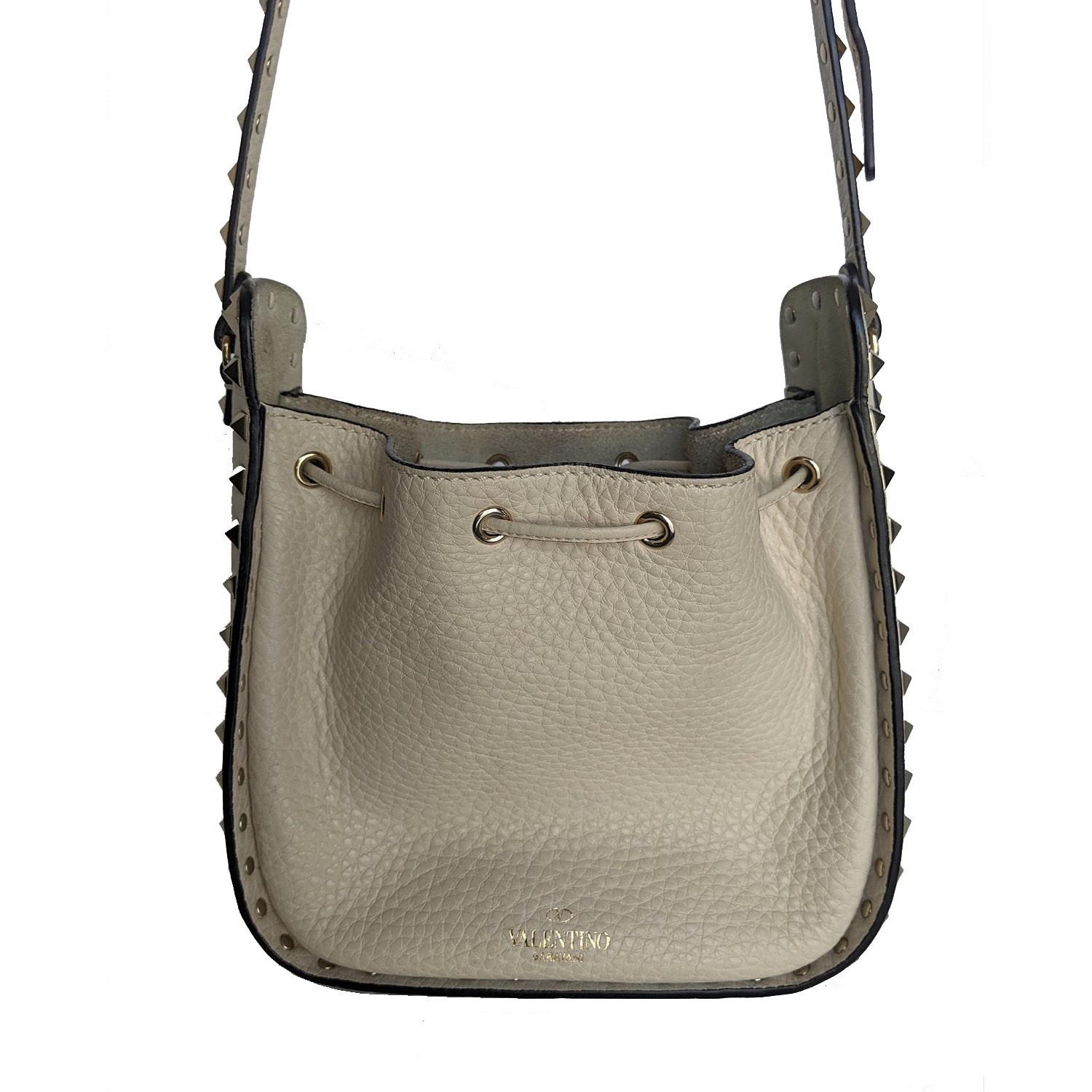 This luxurious bag is crafted of beautifully grained calfskin leather in Ivory with light gold pyramid studs on all borders. The bag features a leather cross body shoulder strap also lined with studs. The shoulder bag opens by a cinch cord to a