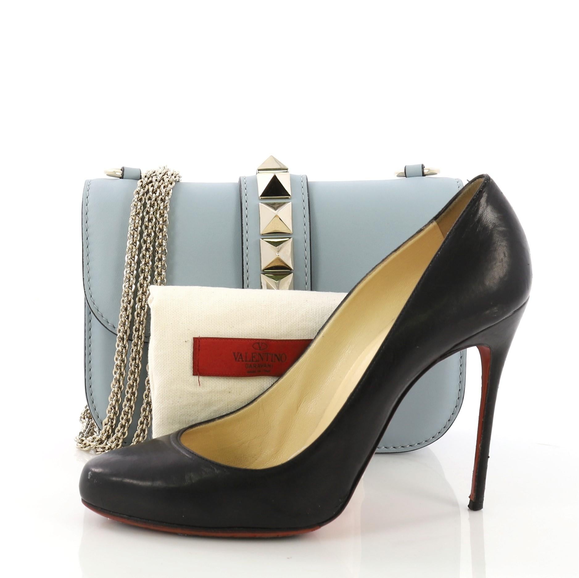 This Valentino Glam Lock Shoulder Bag Leather Small, crafted from light blue leather, features a long chain strap, pyramid studs at the center, and gold-tone hardware. Its push-lock closure opens to a beige fabric interior with side zip and slip