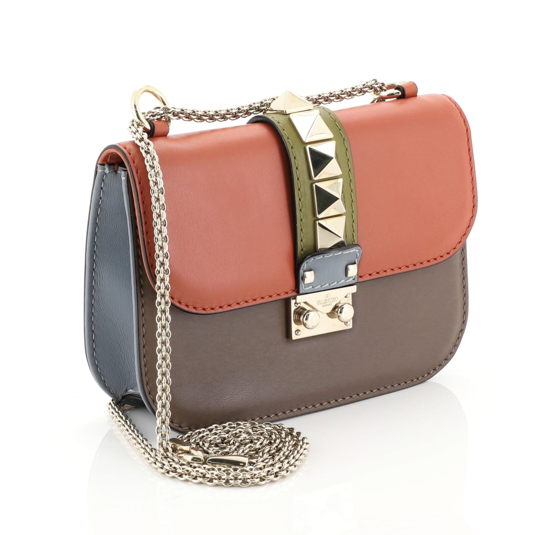 This Valentino Glam Lock Shoulder Bag Leather Small, crafted in multicolor leather, features a chain link strap, pyramid studs, and gold-tone hardware. Its push-lock closure opens to a neutral fabric interior with zip and slip pockets. 

Estimated
