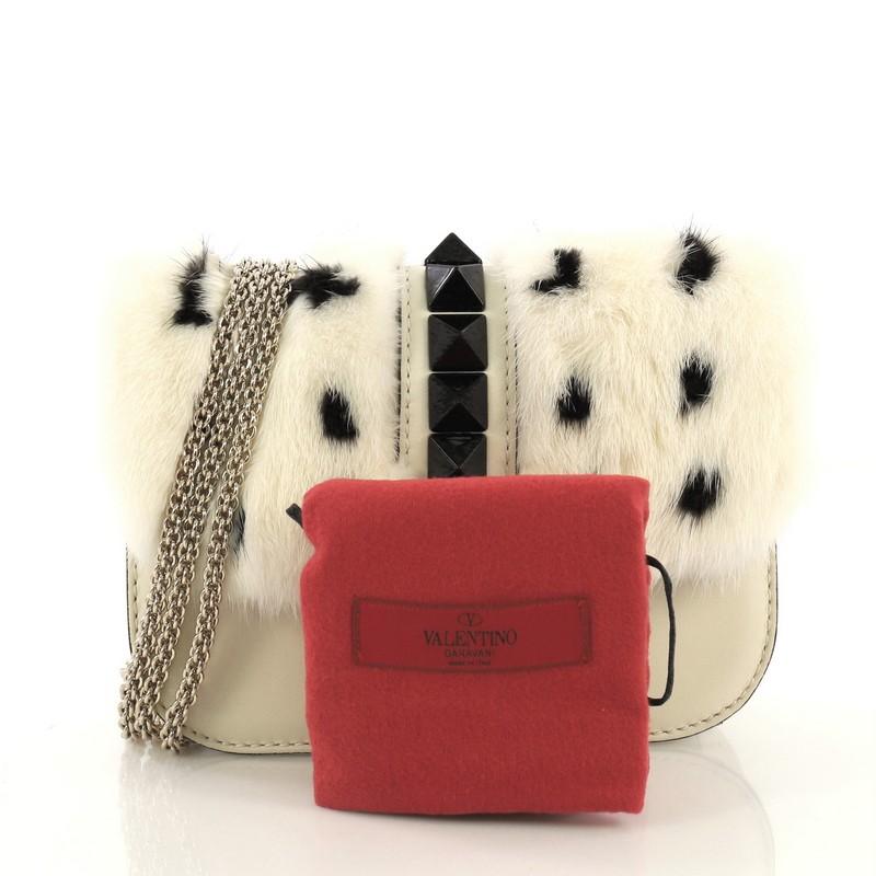 This Valentino Glam Lock Shoulder Bag Mink Small, crafted in off white mink and leather, features a chain link strap, pyramid studs, and gold-tone hardware. Its push-lock closure opens to a black leather interior with zip and slip pockets. This item