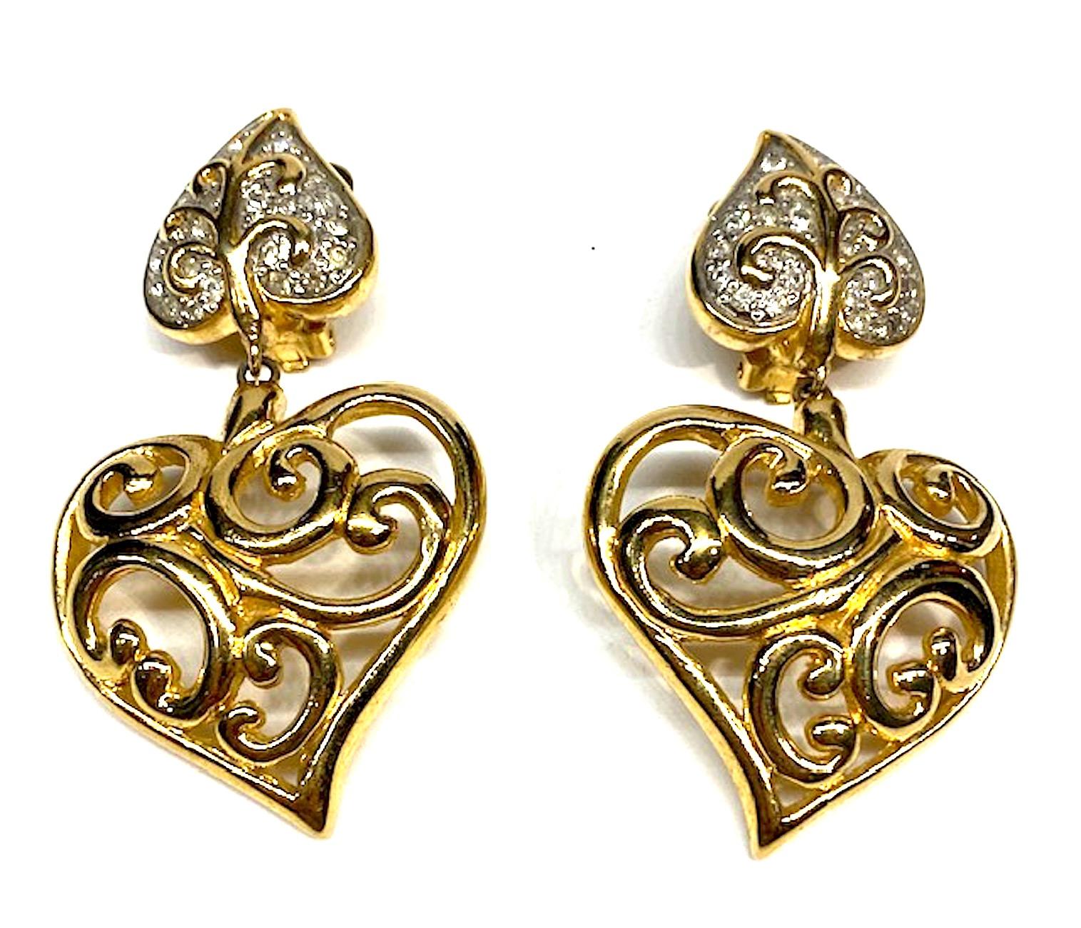 Fancy scrollwork  make up these large Valentino gold tone and rhinestone heart pendant earrings from the 1980s. The top leaf, .88 by 1 inch wide and high, is set with pave' rhinestones. Suspended from the leaf is a 1.63 by 1.5 inch scrollwork gold