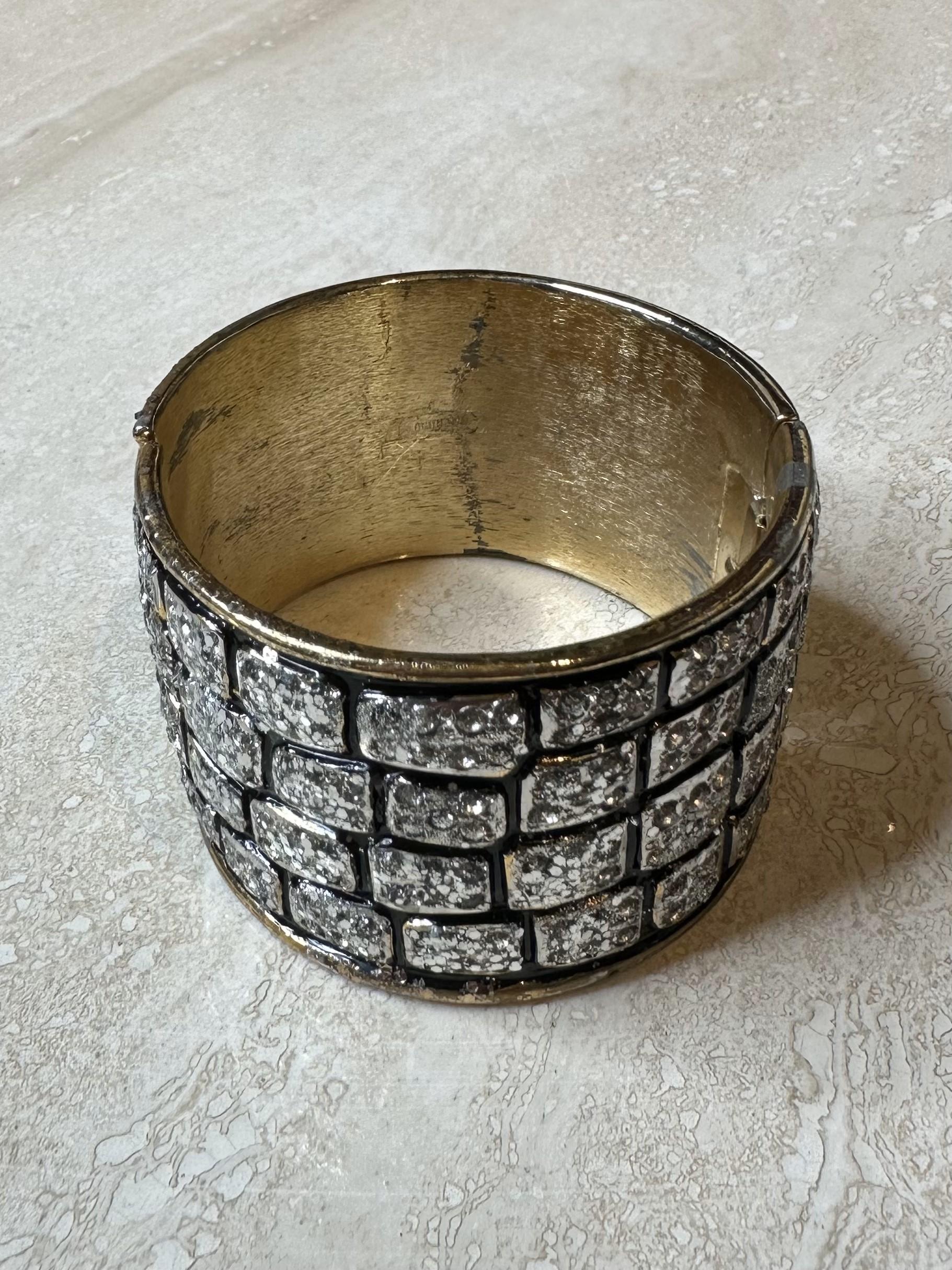 Il bracciale Golden Glitter Brick di Valentino è un gioiello audace, lussuoso e moderno che unisce il fascino architettonico di un design ispirato ai mattoni con il glamour dei glitter dorati. Questo polsino ampio e di grande effetto aggiunge un
