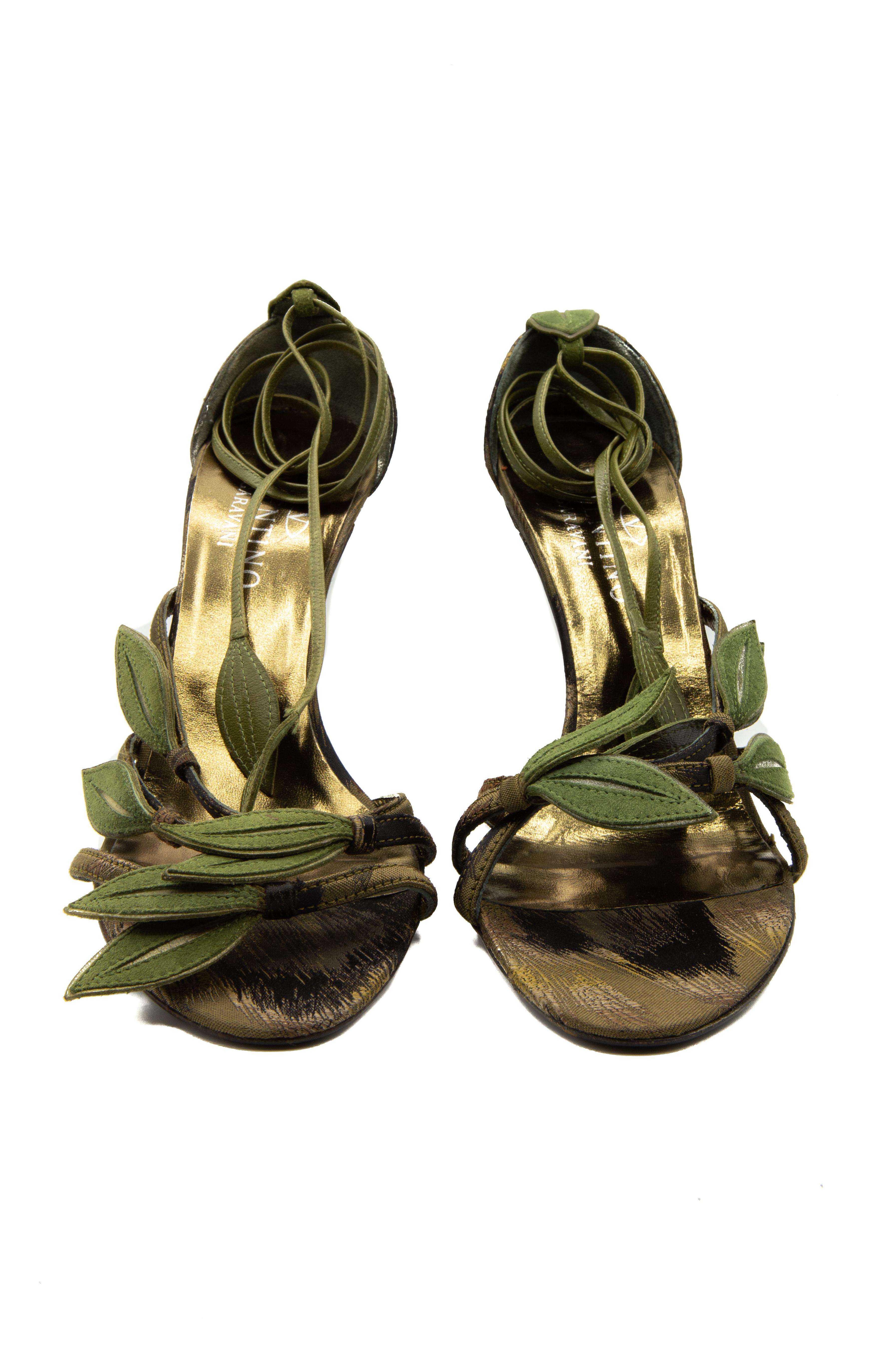 Valentino Garavani Bamboo Sandal Leaf Heel. With stylised ankle straps resembling vines, these pewter sandals give the illusion of vines climbing the wearer's leg. Forest green straps with a metallic copper heel give the heels a feeling that is