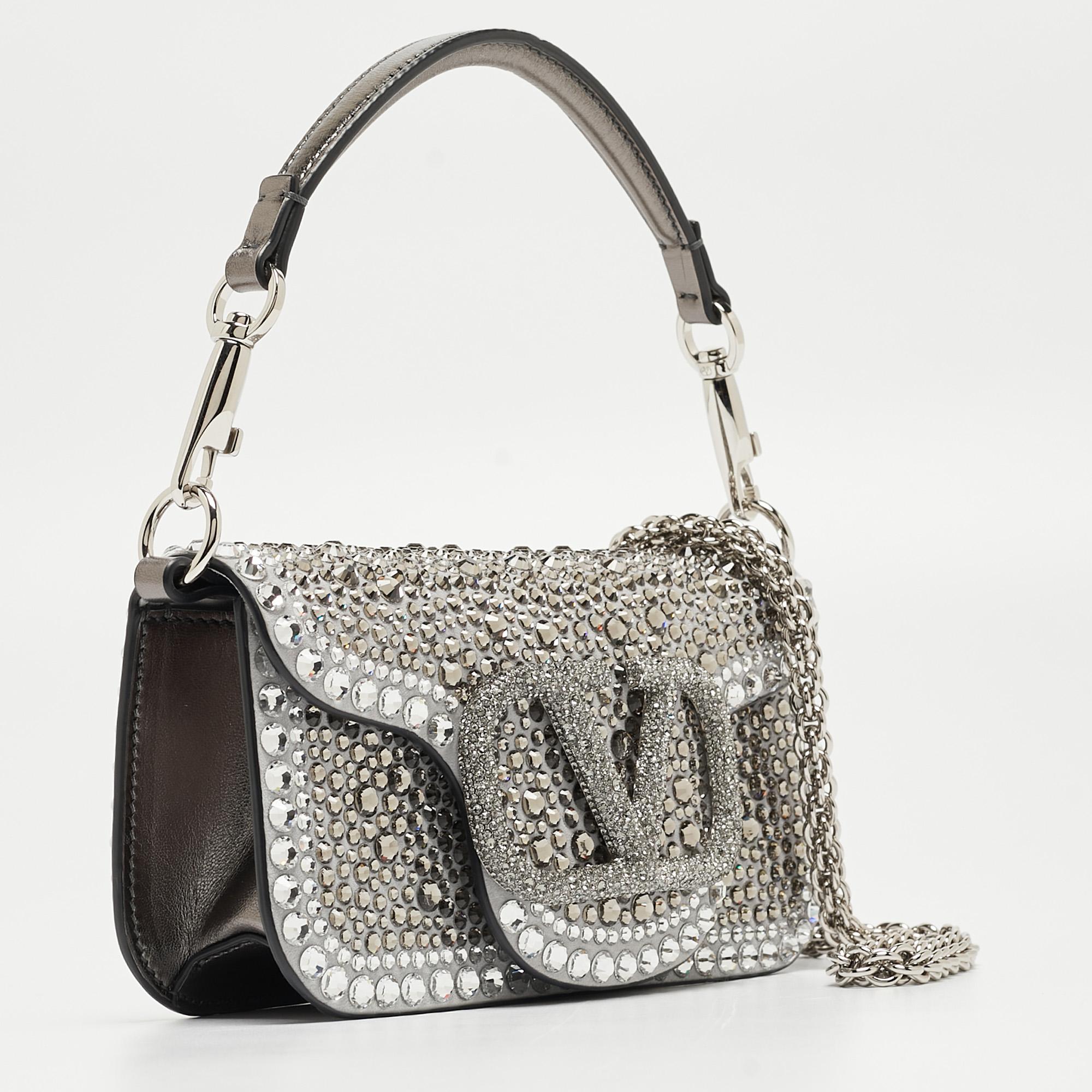 The Valentino VLogo Loco Baguette Bag is a breathtaking blend of sophistication and glamour. Crafted with meticulous attention to detail, its luxurious suede and leather construction is adorned with dazzling crystals, exuding elegance and refinement