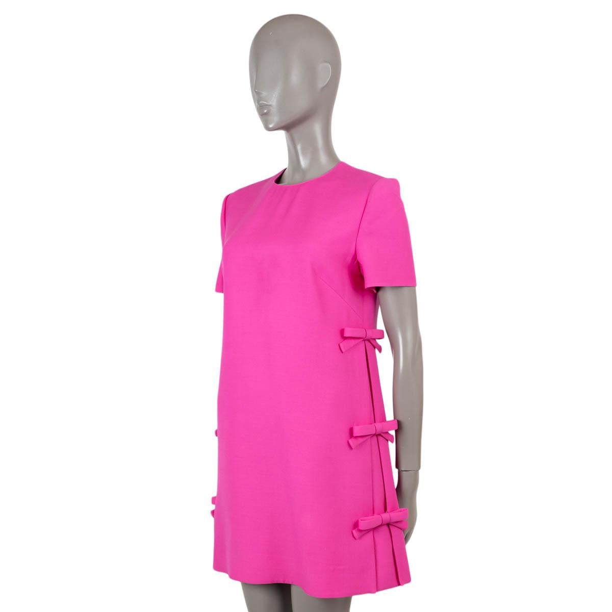 100% authentic Valentino mini dress in hot pink crepe wool (65%) and silk (35%). Features a crewneck, short sleeves and bow embellished side pleats. Opens with hook and concealed zipper in the back and is lined in viscose (with 9% elastane). Has