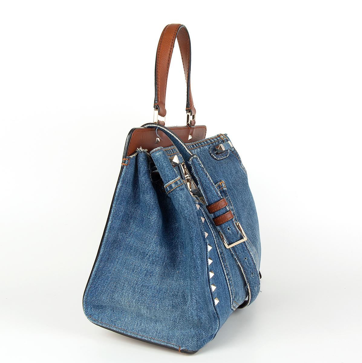 Valentino Garavani 'Joylock' small single handle shoulder bag in blue denim and Stampa Alce calfskin details featuring light gold-tone hardware, front pocket and decorative studs and lock. The bag can be carried by hand thanks to the top single