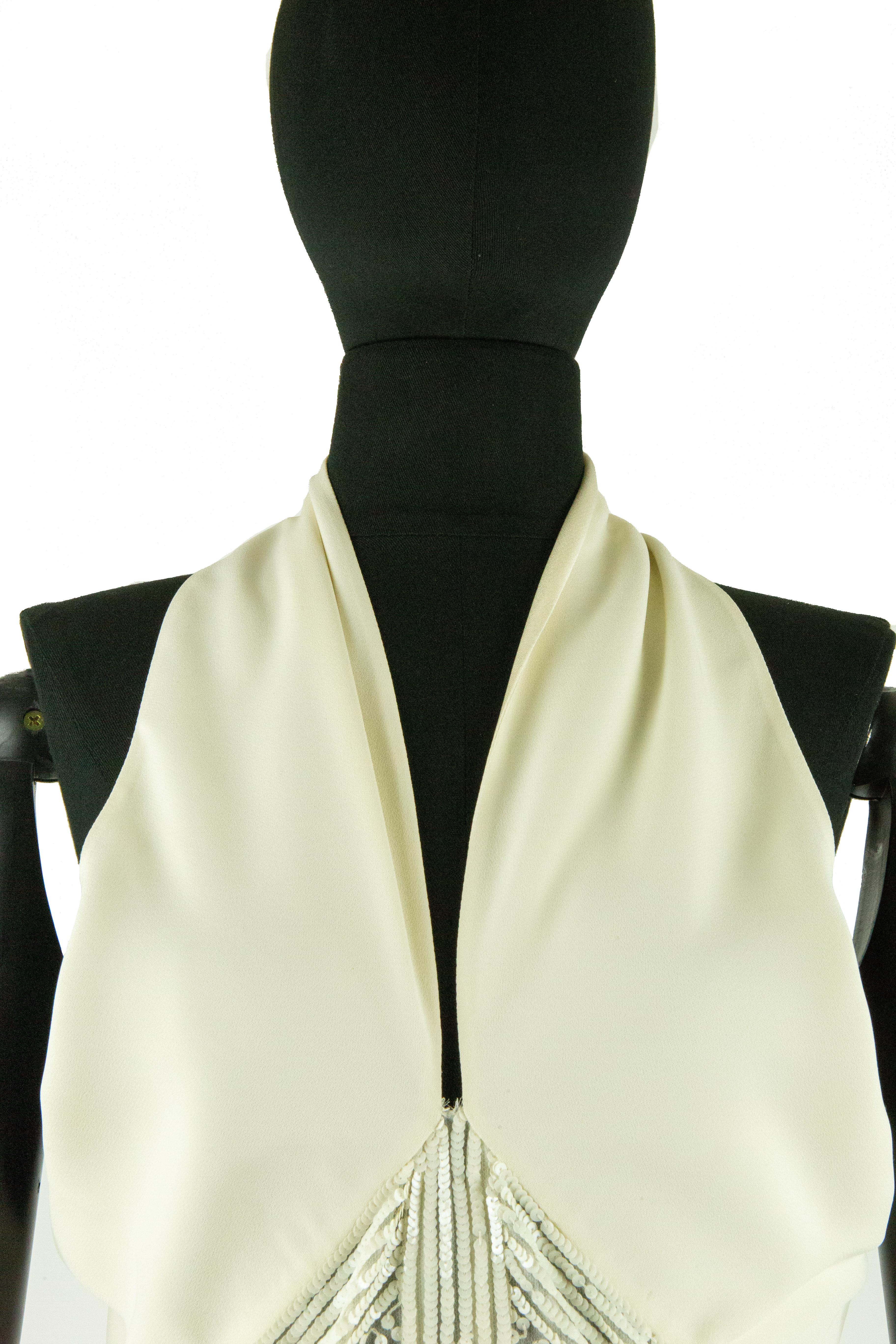 A Valentino ivory crepe de chine cocktail dress with a slouched halter-neck and plunging neckline. The bodice also features an open back and buttons on the back of the neck. The skirt has a pointed empire line below the bust which becomes a straight