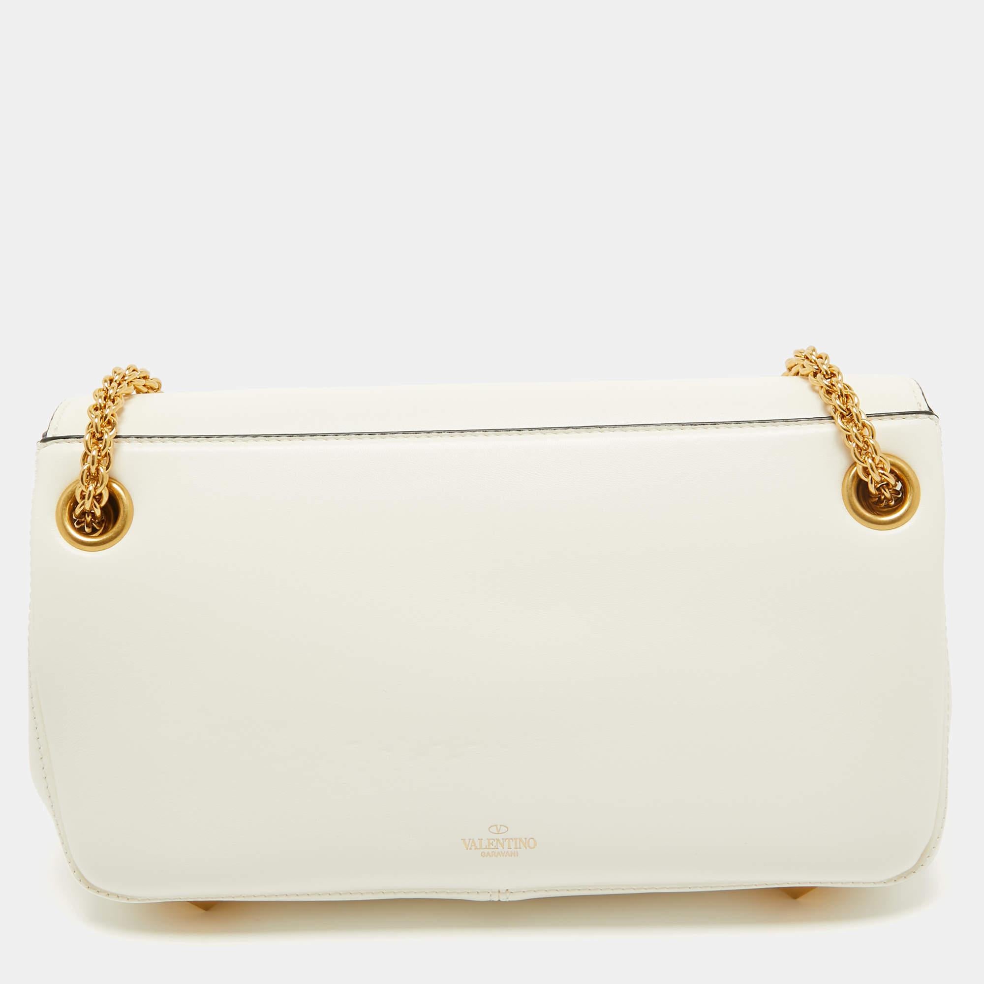 The Valentino bag epitomizes sophistication with its luxurious ivory leather adorned with signature studs. This exquisite accessory features a spacious interior, an adjustable shoulder strap, and the iconic Valentino logo, making it a timeless and