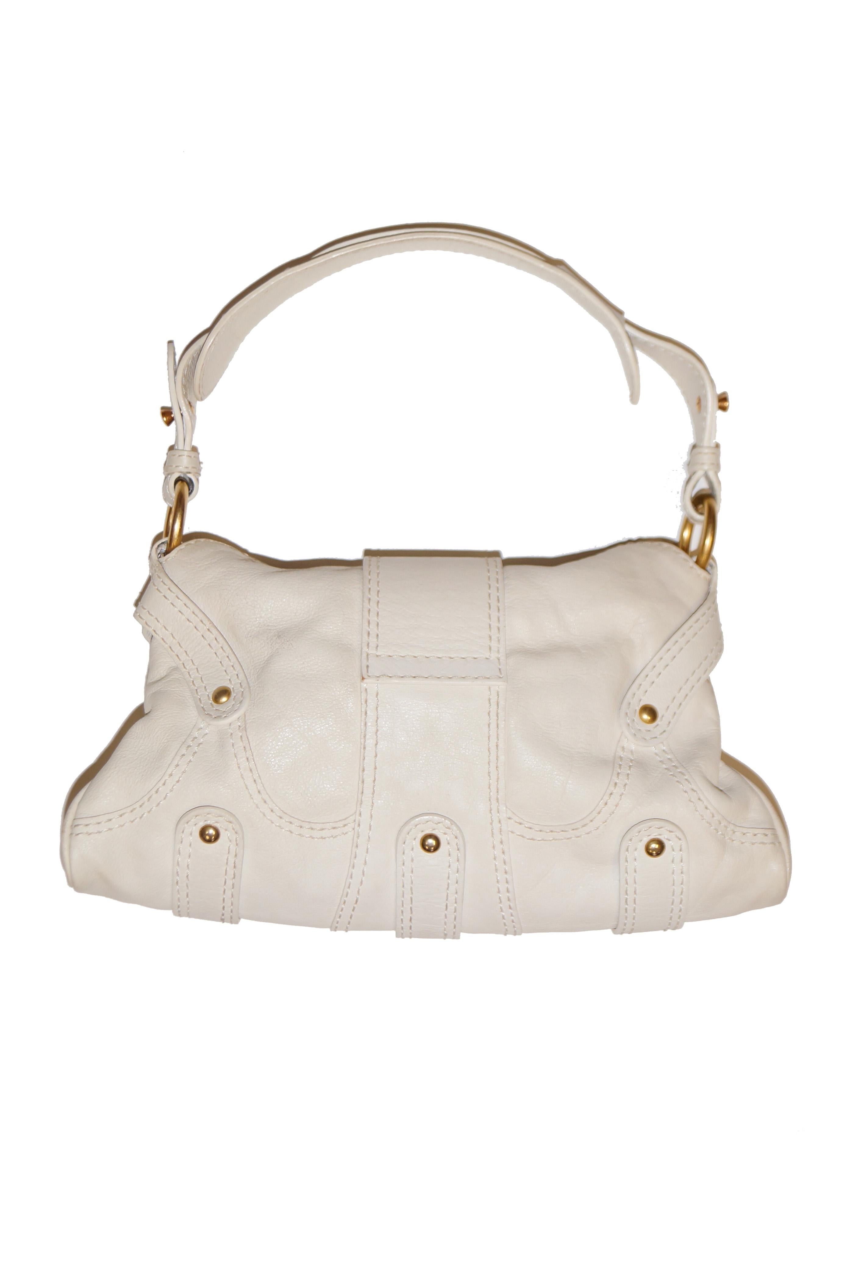 A classic! Delightful soft cream leather baguette handbag by Valentino. The handbag is trapezoid shaped with a zipper closure and flap featuring a bold wooden and gold tone “V” initial with added turquoise stones. Features an adjustable strap with