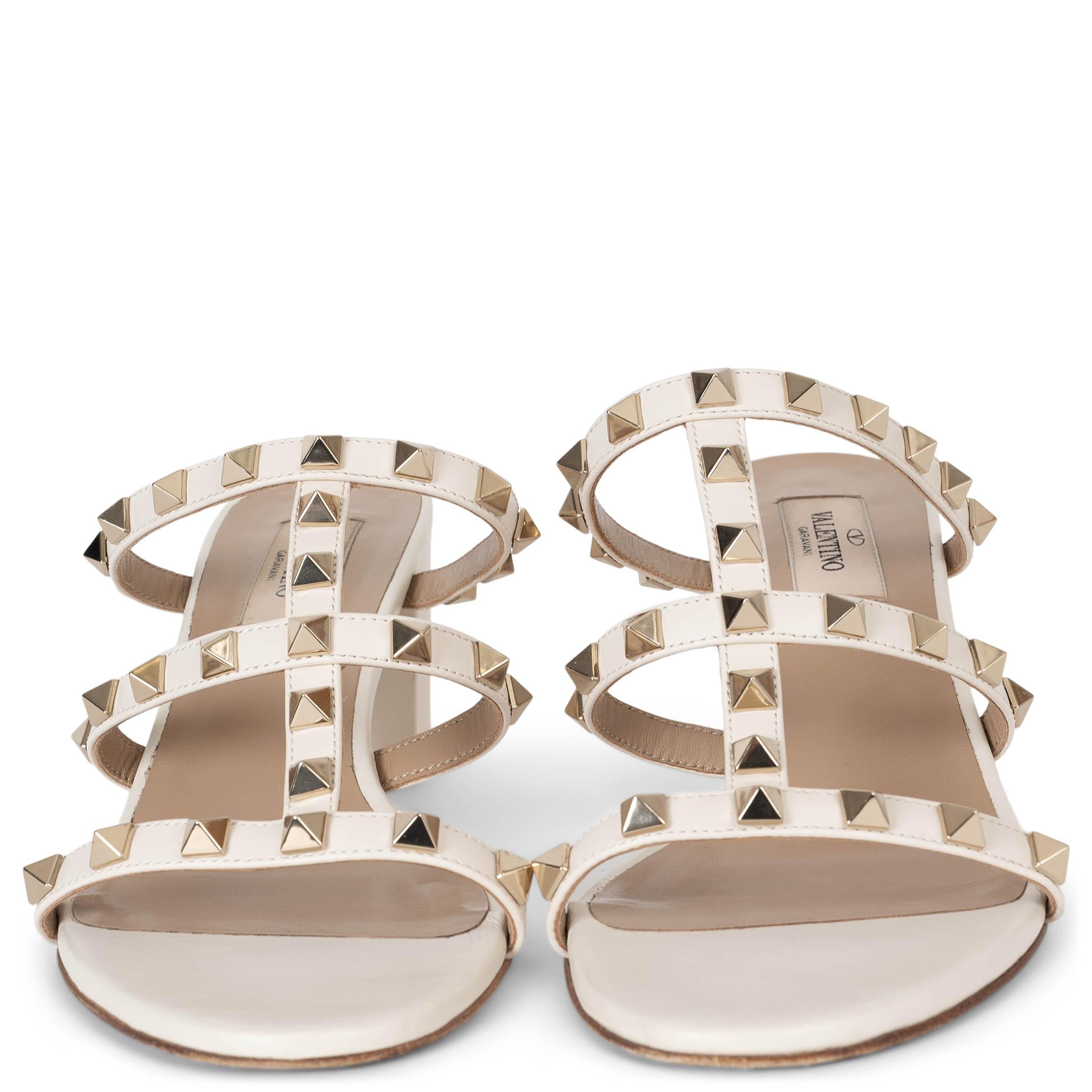 This 100% authentic Valentino Rockstud slide sandals in light ivory leather embody effortless elegance with an edgy touch. Adorned with signature platinum-plated pyramid studs, they feature a sleek, open-toe design with rounded toes and comfortable