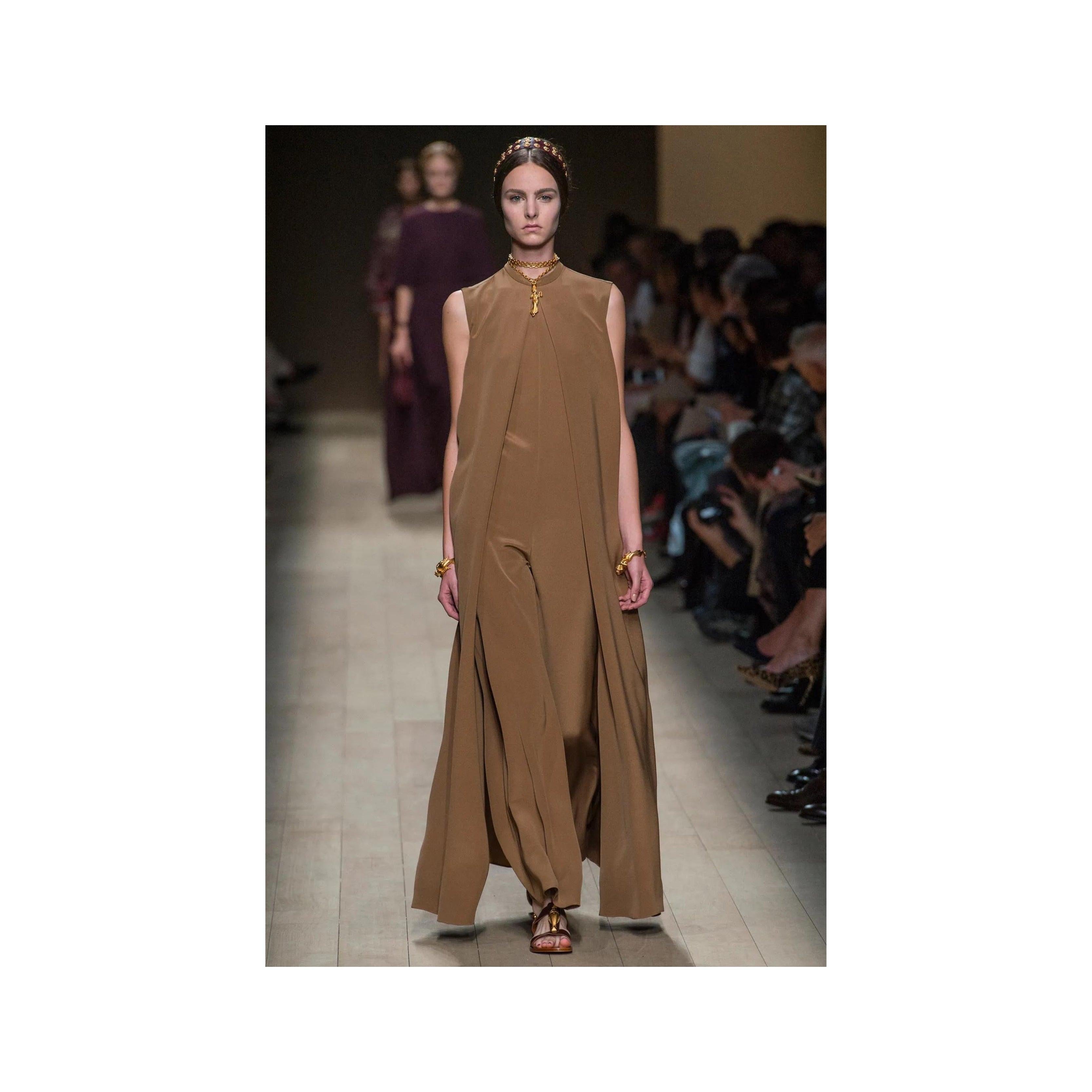 Expertly crafted for the Spring 2014 runway, the Valentino Long Jumpsuit with Cape boasts a high neck and sleeveless design in an elegant dark beige color. The flowing cape falls gracefully from the shoulder, creating a stunning front opening to