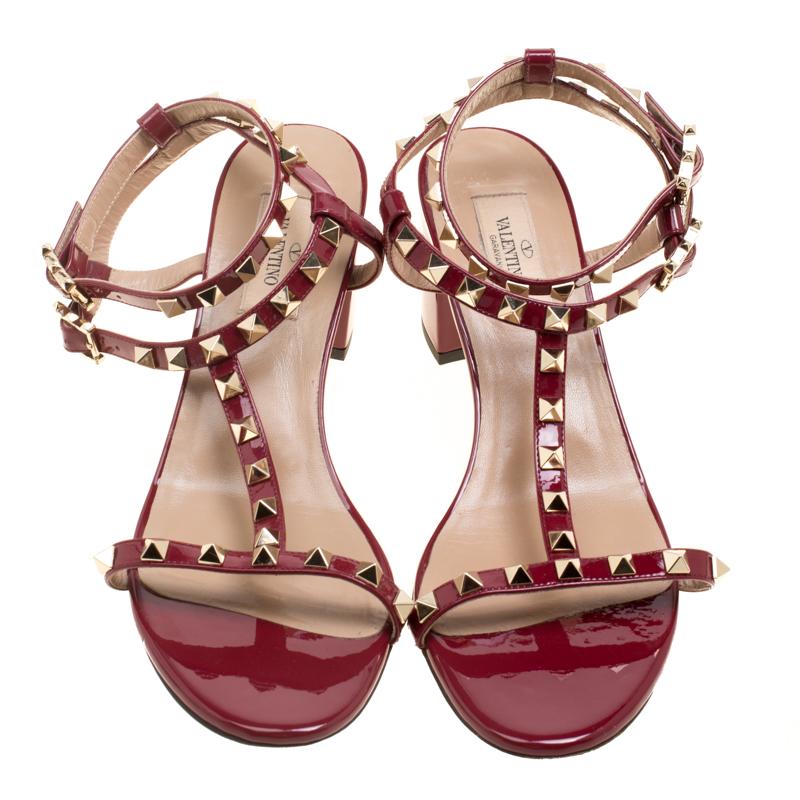 How lovely, elegant and stylish are these maroon sandals from Valentino! They are crafted from patent leather and feature an open toe silhouette. They flaunt a T-strap design with the signature Rockstud detailing, buckled ankle straps, comfortable