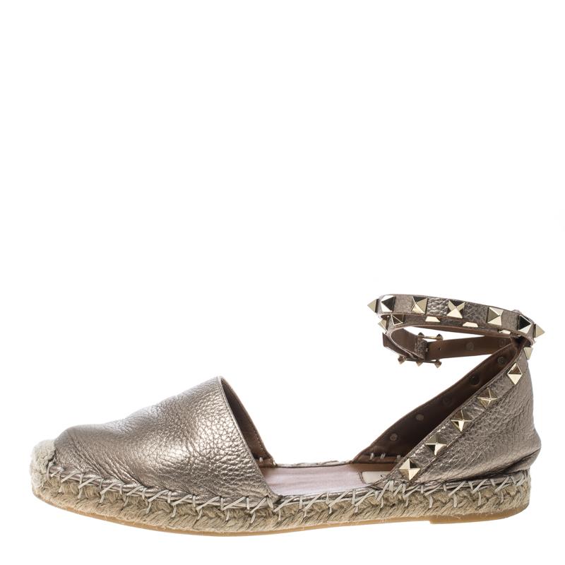 Step out in style with these trendy espadrilles from Valentino. Featuring a metallic beige shade with closed toes, ankle wraps featuring the signature pyramid studs, and braided detailing on the midsoles, these flats are sure to stand out this