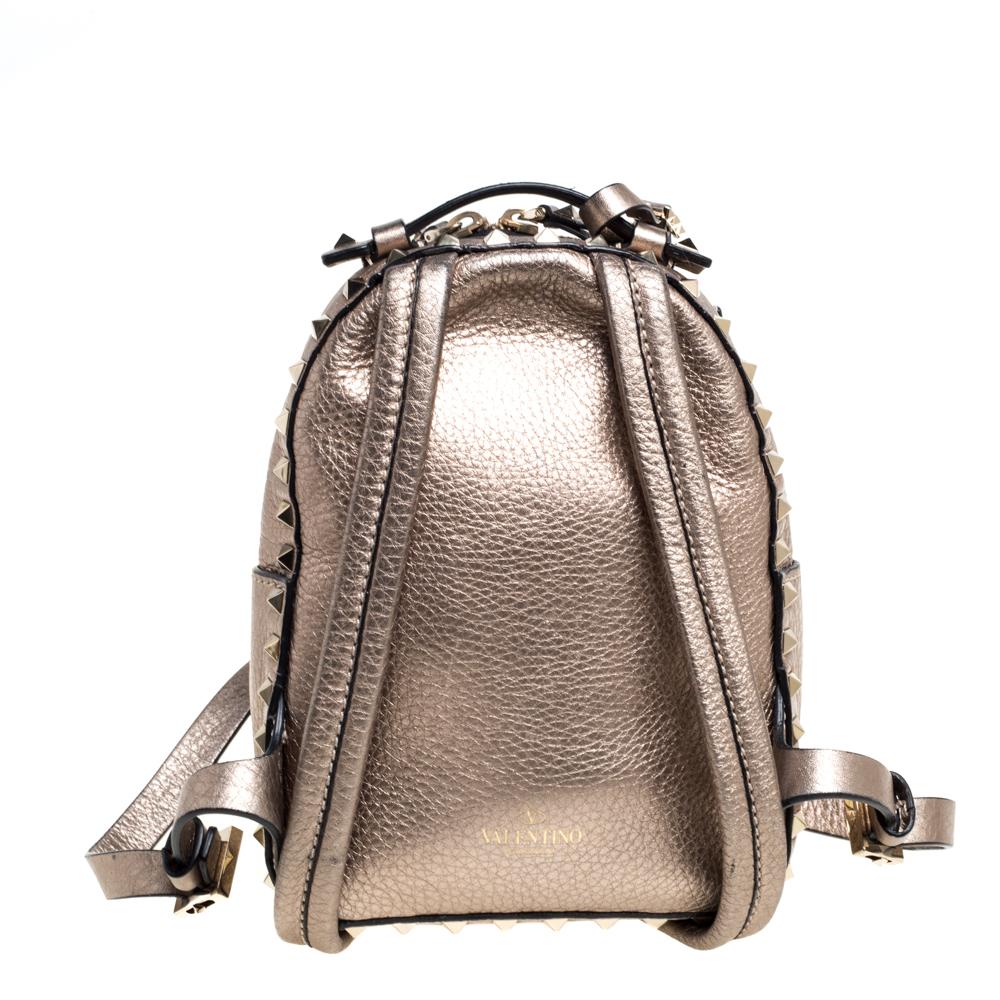 This petite Rockstud backpack from Valentino is a must-have! Crafted in Italy, the bag is made from metallic light brown leather and decked with signature pyramid studs. It has two adjustable straps, a suede interior lining, and a front zipped