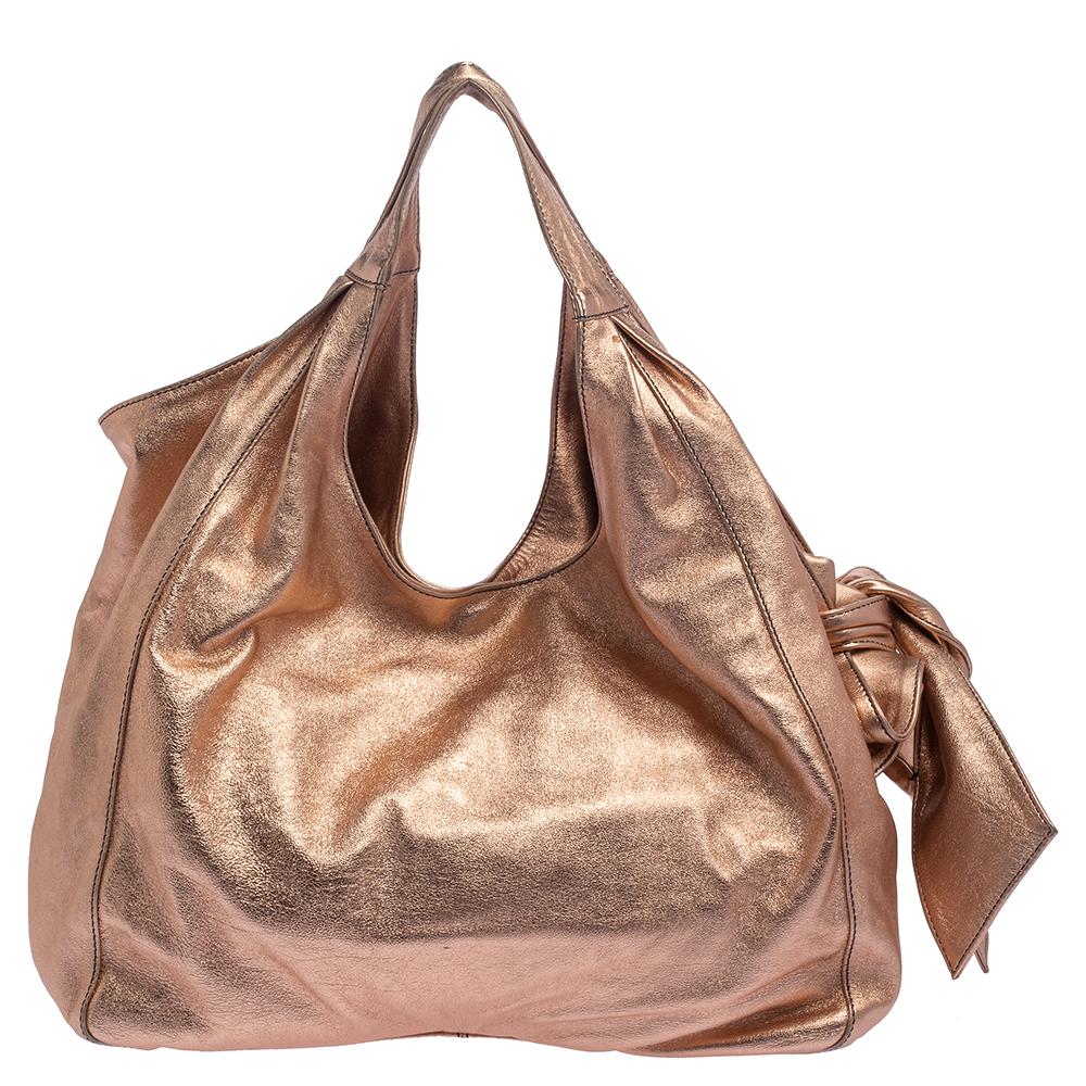 The signature Valentino bow on the side is the highlight of this Nuage Bow tote. It is crafted using metallic rose gold leather and equipped with two handles and a spacious fabric interior. This eye-catching bag will add a chic finish to your