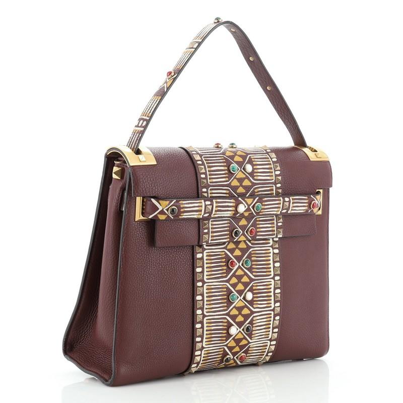 This Valentino My Rockstud Satchel Tribal Embellished Leather Medium, crafted in red leather with tribal pattern embellishments, features single loop leather handle, multiple stud detailing, and aged gold-tone hardware. Its flap closure opens to a
