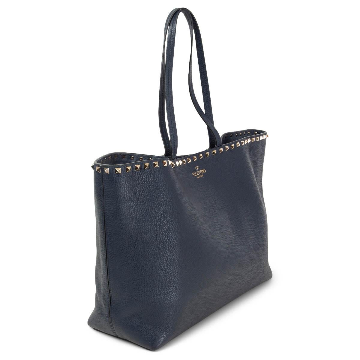 100% authentic Valentino Garavani Rockstud tote bag in dark blue grainy calfskin leather. Top edge adorned with platinum studs. Opens with a magnetic closure on top and is unlined. Flat zipper pocket and double slip pocket inside. Has been carried