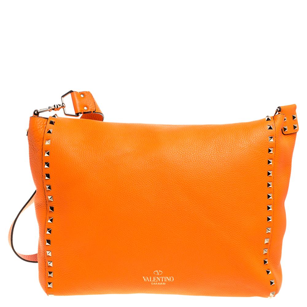 This stylish Valentino messenger bag comes made from leather and designed with the signature Rockstuds in gold-tone all over the exterior. It features a bright neon orange hue and buckled straps on the front. It also comes with a broad shoulder