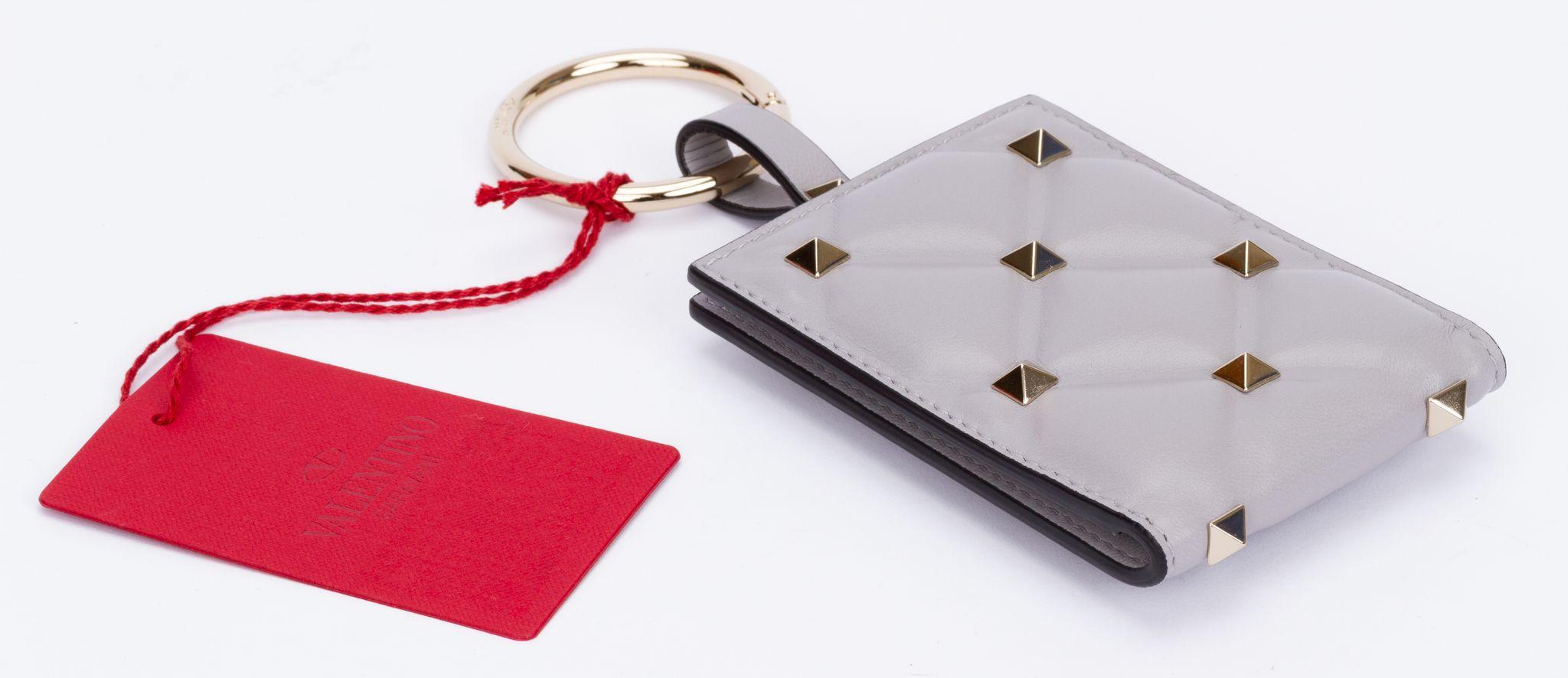 Porte-clés Valentino avec une breloque carrée en cuir gris qui comprend un miroir. Fonctionne également comme portefeuille de cartes de crédit. L'anneau est en argent. La pièce est neuve et est livrée avec l'étiquette, les livrets, la boîte