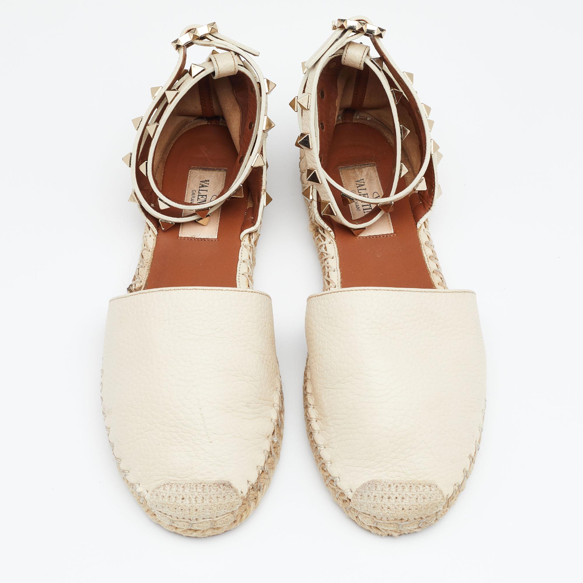 Step out in style with these trendy espadrille flats from Valentino. Featuring a shade of off-white with closed toes, ankle wraps with signature Rockstuds, and braided detailing on the midsoles, these flats are sure to stand out this season. They