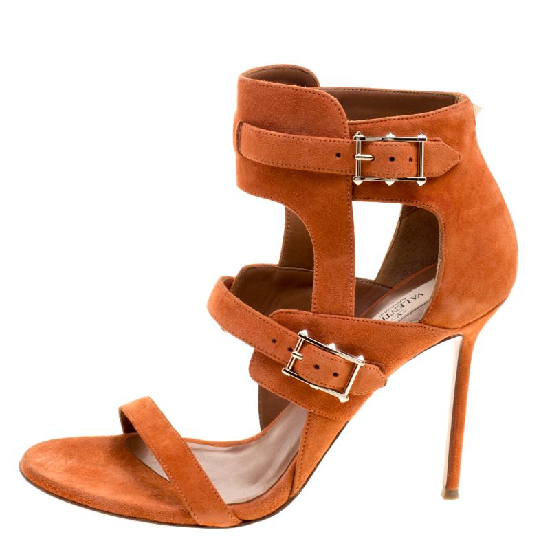 Beautifully designed in bright and beautiful orange suede leather, these Valentino wrap sandals are perfect to wear at both day and night time occasions. These sandals feature a front strap and dual silver-tone buckled top straps that go up till