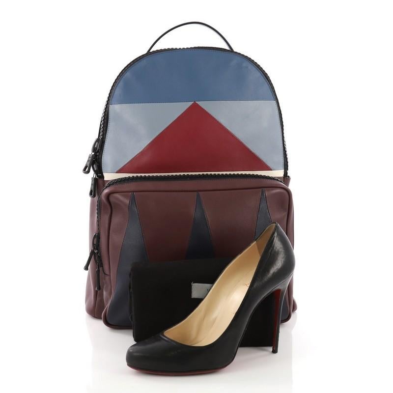 This Valentino Patchwork Backpack Leather Large, crafted from burgundy and blue leather, features adjustable backpack straps, geometric design, front zip pocket, and black-tone hardware. Its zip closure opens to a burgundy leather interior with slip