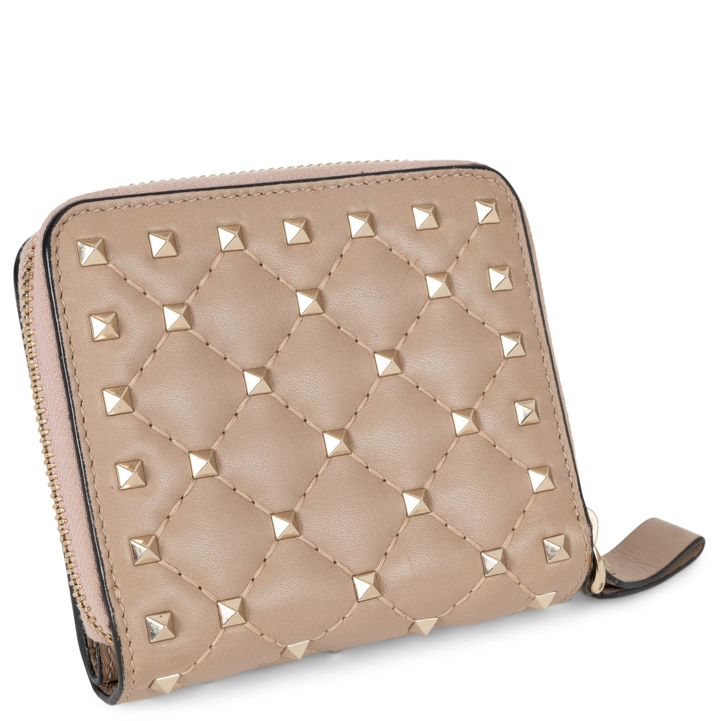 Ce portefeuille compact Valentino Rockstud Spike, 100% authentique, est confectionné en cuir Poudre (nude) matelassé et rehaussé des clous pyramidaux dorés clairs signature. Il comporte d'un côté une pochette zippée pour la monnaie, tandis que