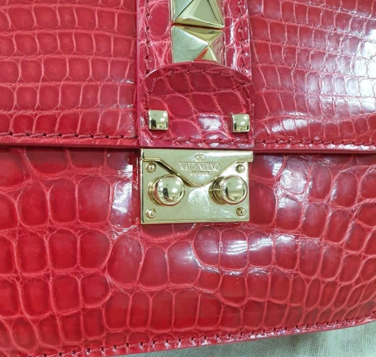 Crafted from exotic crocodile skin, this red piece comes with a gold-tone chain and a flap with a push-lock to secure the well-sized interior. 
The bag is joined in harmony by the brand's famous Rockstuds.

Includes: Original Dustbag
Length-20