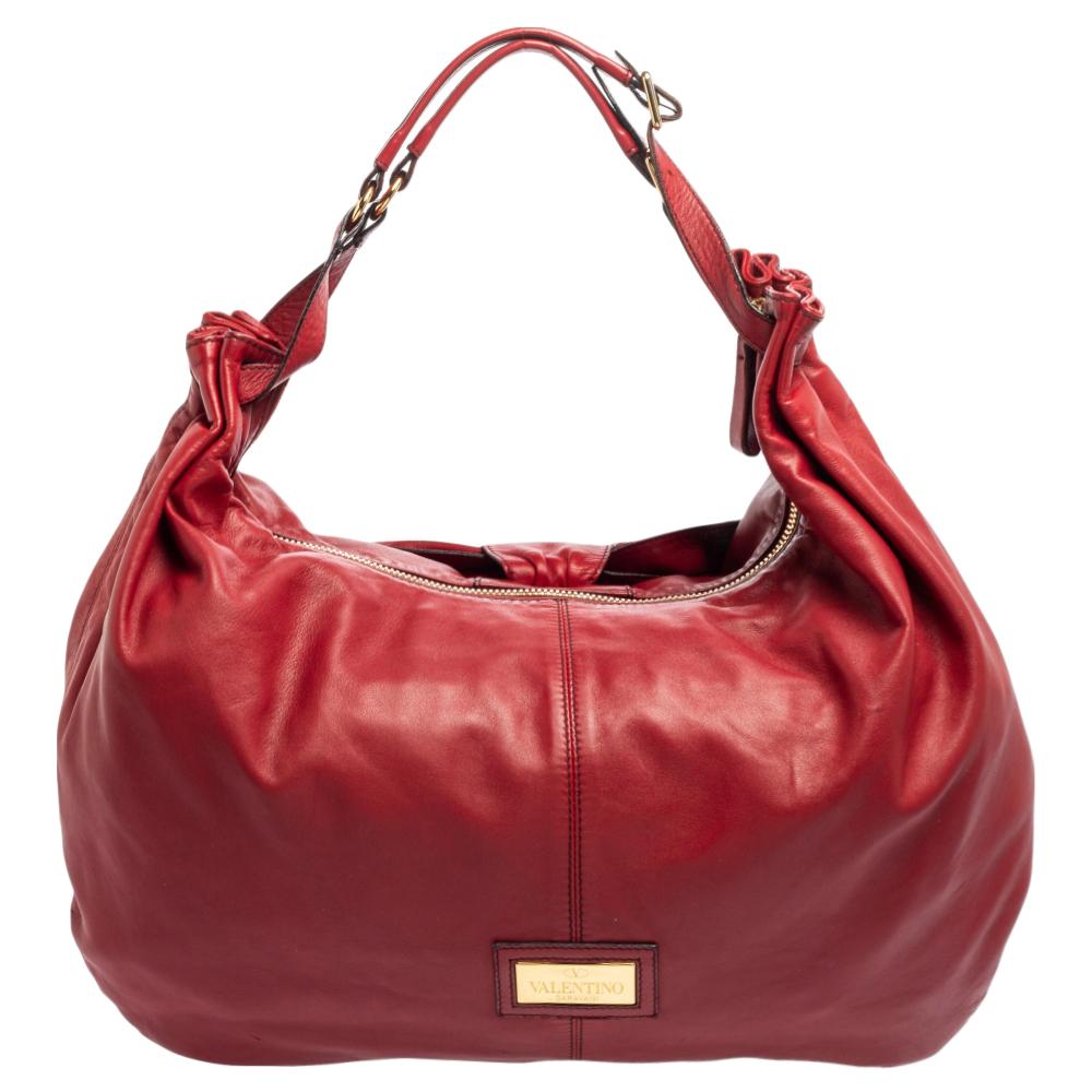 The bow at the front is the highlight of this Valentino hobo. It is crafted using red leather and equipped with a single handle and a spacious satin interior. This eye-catching bag will add a chic finish to your favorite looks.