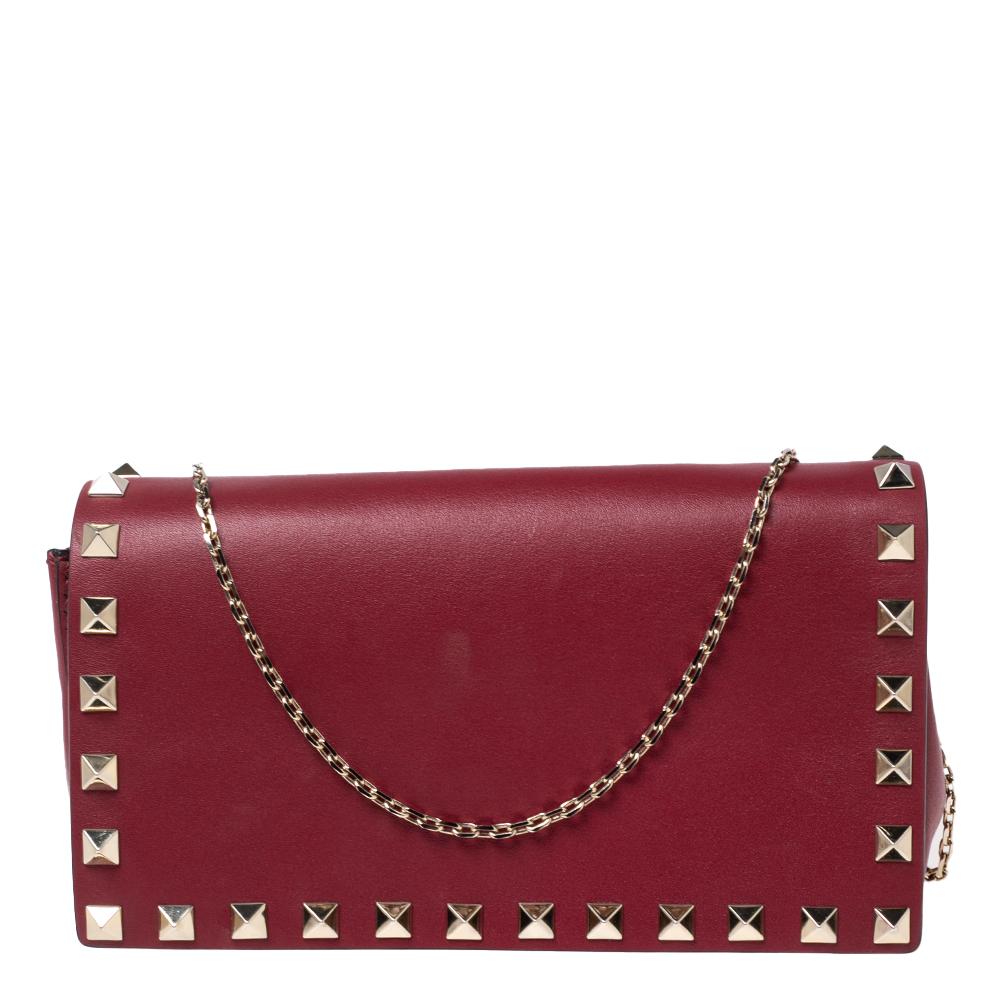 This stunning clutch bag by Valentino is a great example of the brand's exquisite craftsmanship and design aesthetic. It is made from quality leather and comes in a lovely red hue. It is styled with Rockstuds on the exterior and a front flap that