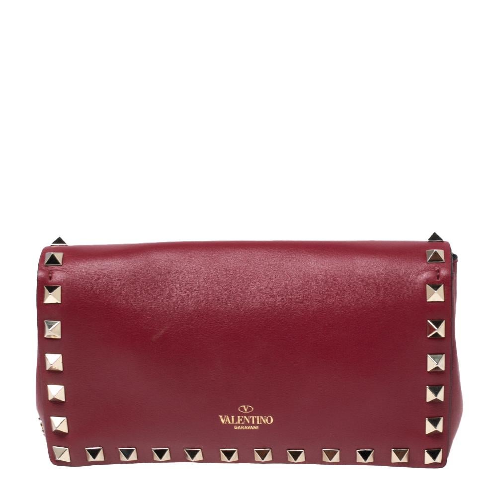 This stunning clutch bag by Valentino is a great example of the brand's exquisite craftsmanship and design aesthetic. It is made from quality leather and comes in a lovely red hue. It is styled with Rockstuds on the exterior and a front flap that