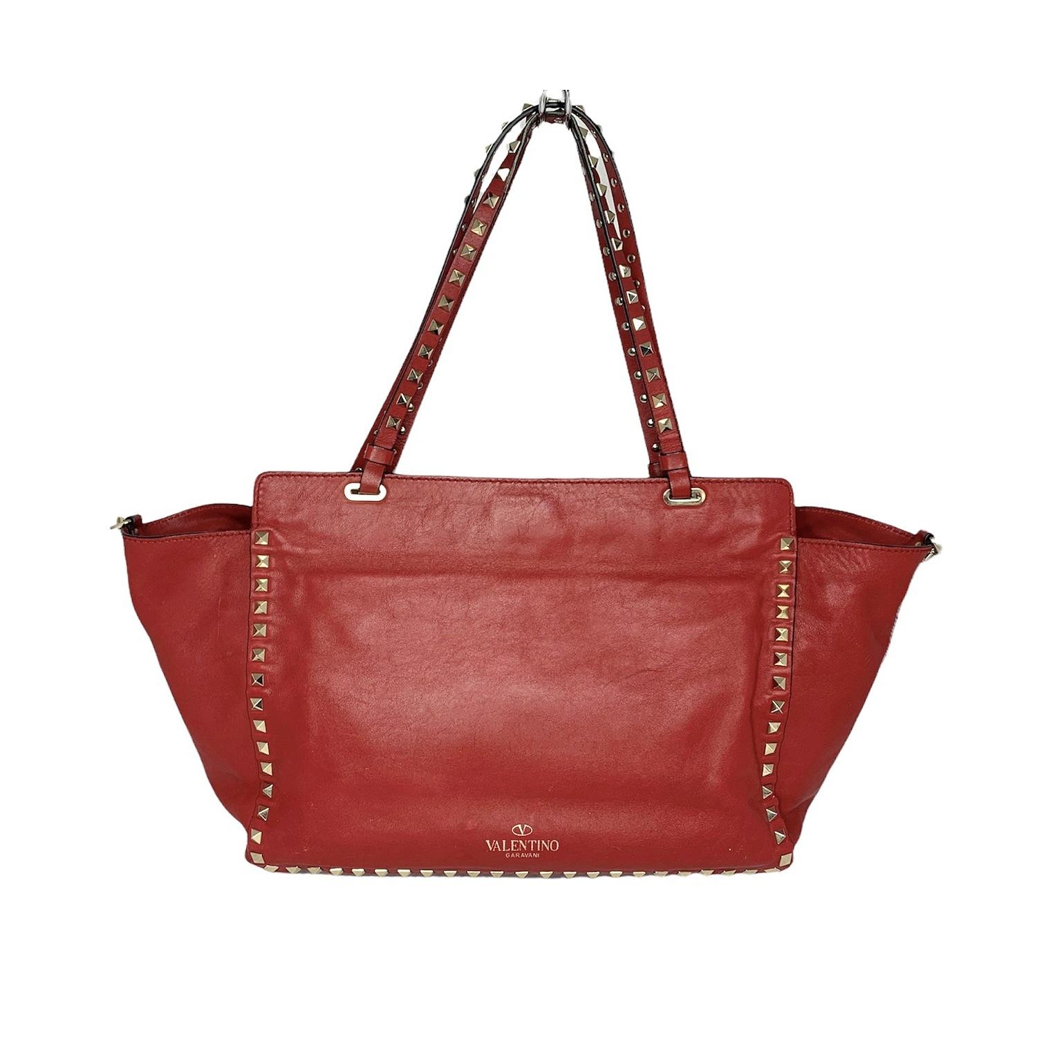 This chic and edgy handbag is crafted of rich calfskin in red. This shoulder bag features signature polished gold pyramid studs along the borders of the bag, the handles, and optional shoulder strap. The top is secured with a fold-over clasp and