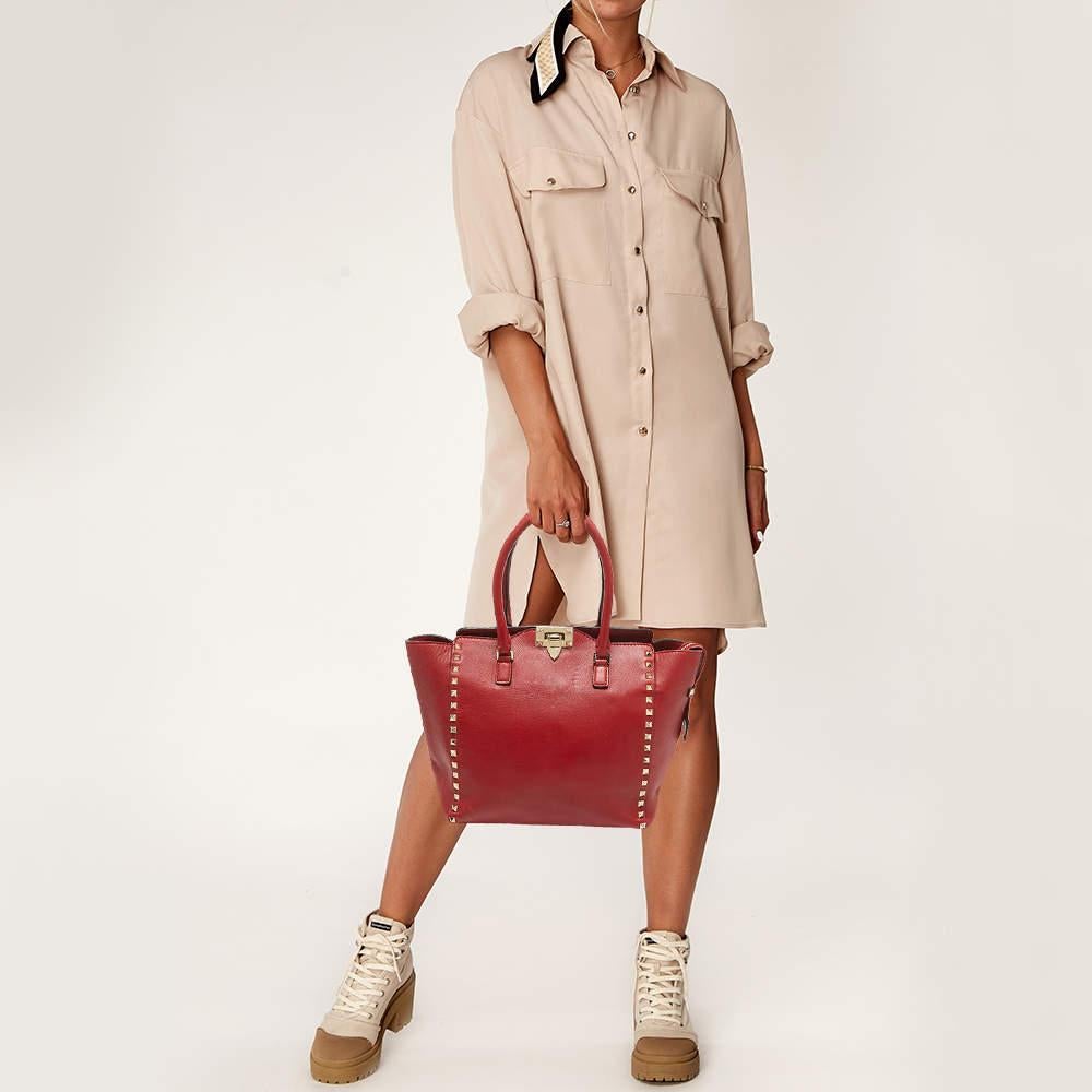 Luxury Italian fashion house Valentino is famed for its classic designs infused with its own signature modern edge and Rockstud details  as showcased by this Trapeze tote. Crafted from leather  it features double top handles accented with gold tone