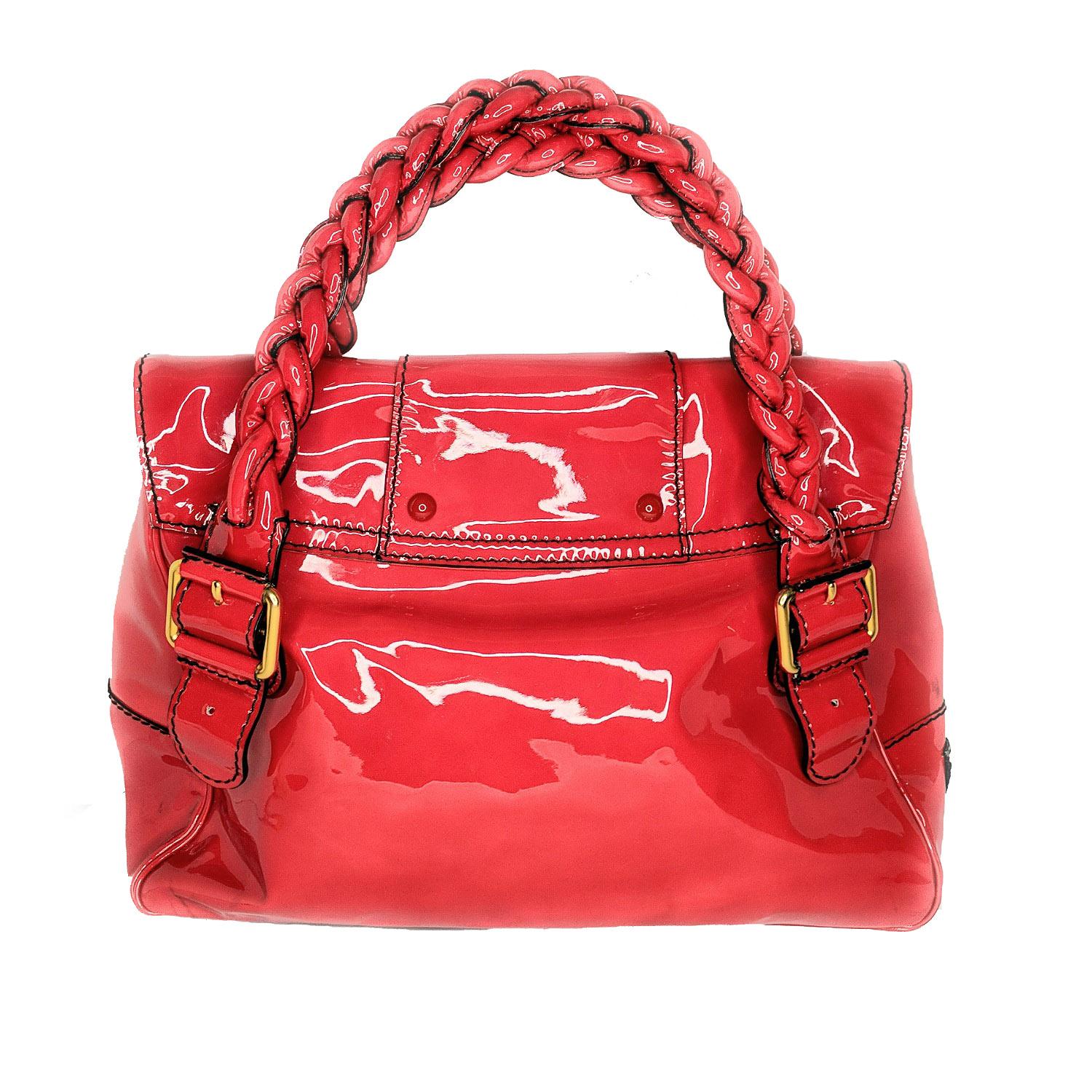 This is crafted of shiny patent leather in red. The bag features braided top handles and strap closures with two facing flap pockets and a cross over flap with a strap. This opens to a fabric interior with room for your everyday essentials with the