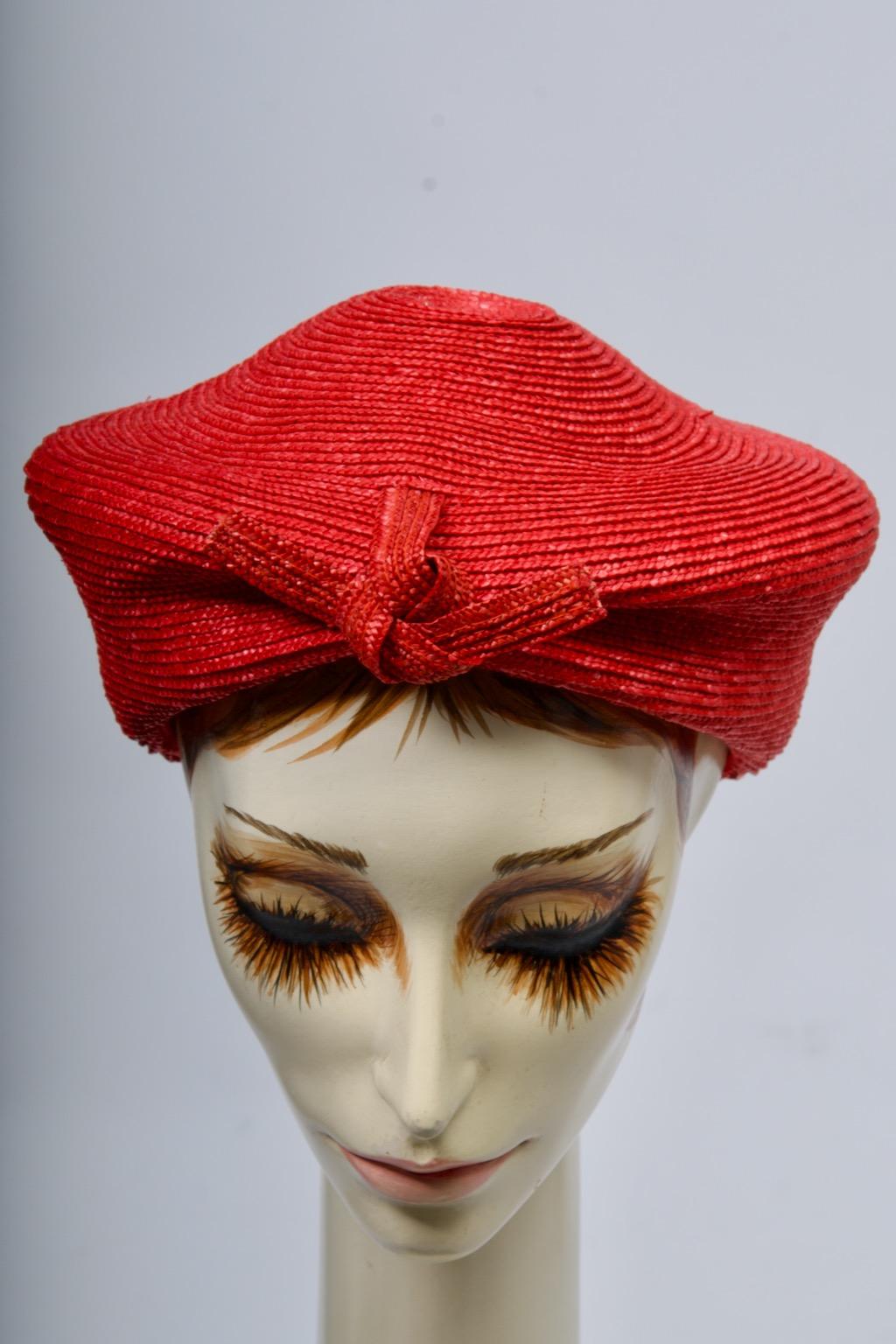 Chapeau de paille rouge Valentino, le dos profond se rétrécissant vers l'avant, où il est plissé au milieu et retenu par un nœud de paille et une cravate. La paille est travaillée en cercles concentriques et est légèrement relevée au niveau de la
