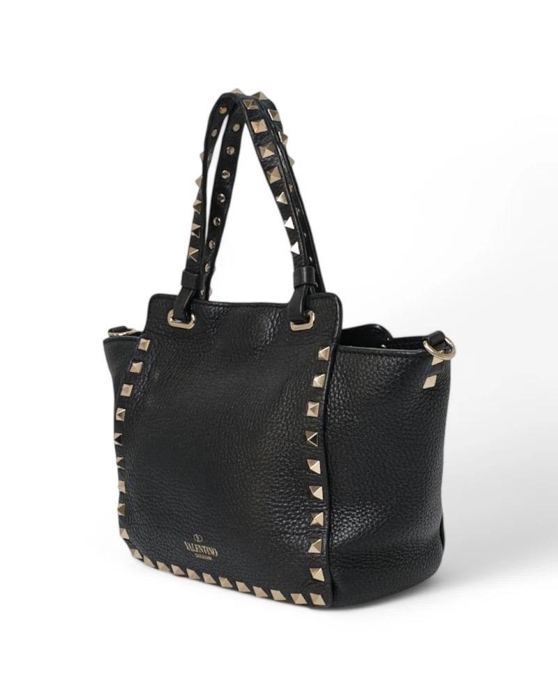 Borsa firmata Valentino, modello Rockstud nella misura small, realizzata in pelle granulata nera e arricchita da borchie applicate con hardware dorato. Dotée d'un chiusura ad incastro, internamente rivestita in tessuto scamosciato tono su tono con