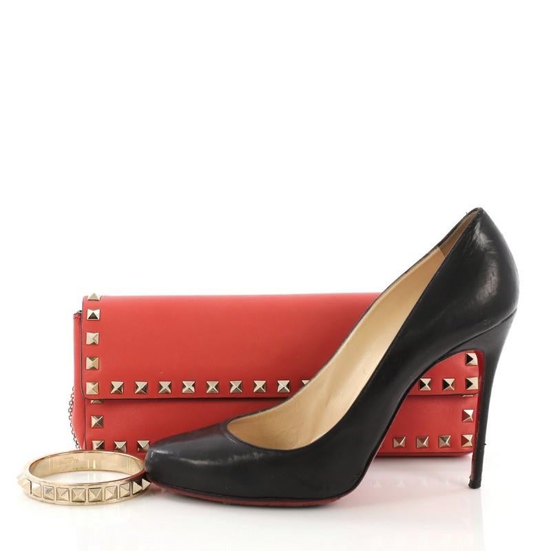 This Valentino Rockstud Bracelet Clutch Leather Long, crafted in red leather, features pyramid stud trim, stud bracelet attached by a chain link, and gold-tone hardware. Its magnetic snap button closure opens to a beige fabric interior with slip