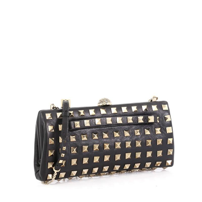 This Valentino Rockstud Chain Frame Clutch Full Studded Leather Small, crafted from black studded leather, features chain link strap, pyramid stud embellishments, front hand strap and gold-tone hardware. It opens to a black leather interior.