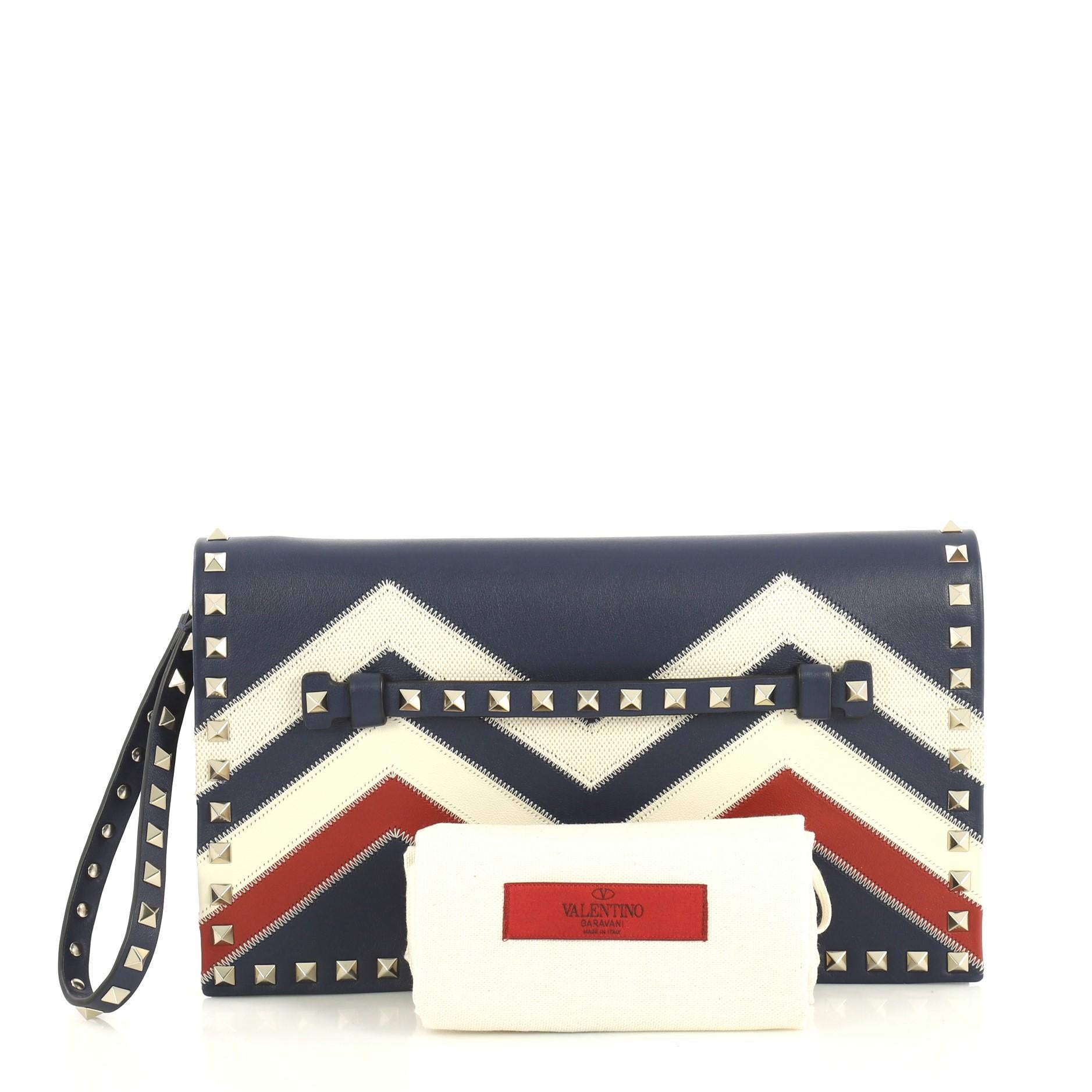 This Valentino Rockstud Flap Clutch Chevron Leather and Canvas, crafted from blue leather and multicolor canvas, features a leather hand sling, studded hand strap, rockstud trim, and gold-tone hardware. Its magnetic snap closure opens to a blue