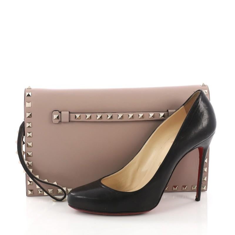 This Valentino Rockstud Flap Clutch Leather, crafted from pink leather, features a leather hand sling, studded hand strap, rockstud detailing, and gold-tone hardware. Its magnetic snap closure opens to a red leather interior showcasing two open