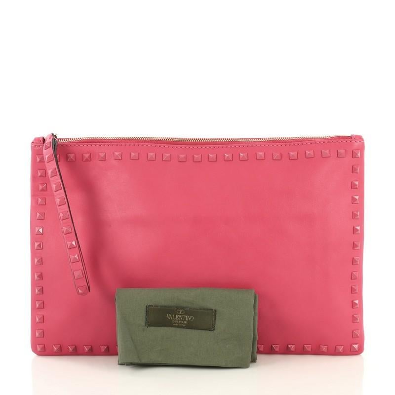 This Valentino Rockstud Pouch Leather Large, crafted from pink leather, features rockstud detailing and gold-tone hardware. Its zip closure opens to a neutral fabric interior with zip and slip pockets. 

Estimated Retail Price: $1,395
Condition: