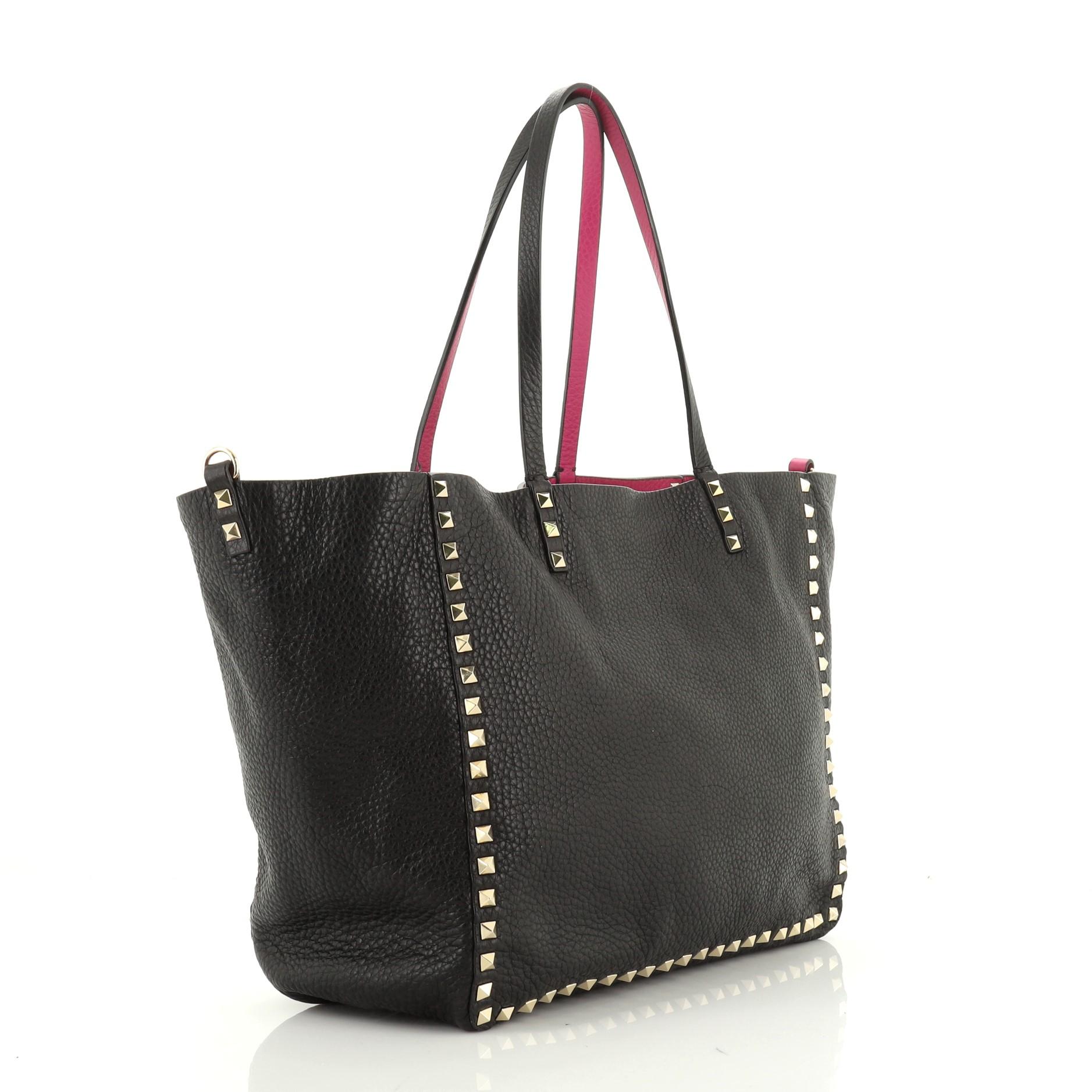 This Valentino Rockstud Reversible Convertible Tote Leather Medium, crafted from black leather, features pyramid rockstud detailing, dual tall flat handles, and gold-tone hardware. It opens to a reversible purple leather interior. 

Estimated Retail