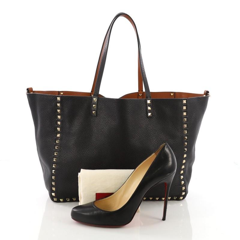 This Valentino Rockstud Reversible Convertible Tote Leather Medium, crafted in black and brown reversible leather, features pyramid rockstud detailing, dual tall flat handles, and gold-tone hardware. Its wide open top opens to its reversible leather