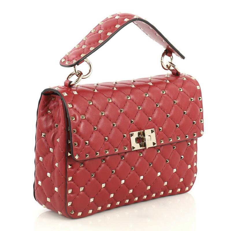 This Valentino Rockstud Spike Flap Bag Quilted Leather Medium, crafted from red quilted leather, features a leather top handle, chain link strap, pyramid stud detailing, and gold-tone hardware. Its turn-lock closure opens to a red leather interior