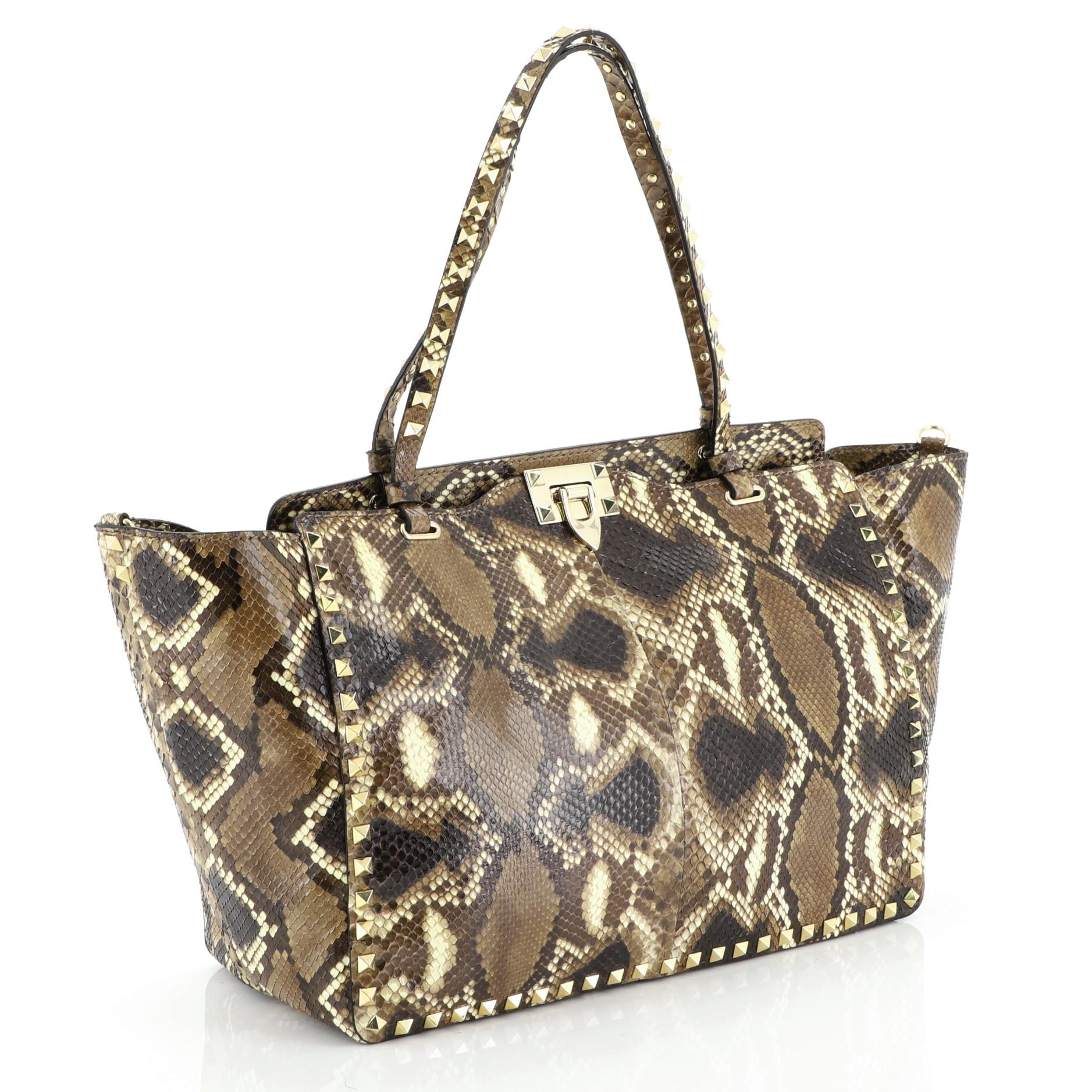 This Valentino Rockstud Tote Python Large, crafted from genuine brown python skin, features dual tall flat handles, pyramid stud details and gold-tone hardware. Its clasp closure opens to a neutral fabric interior with zip pocket. This item can only