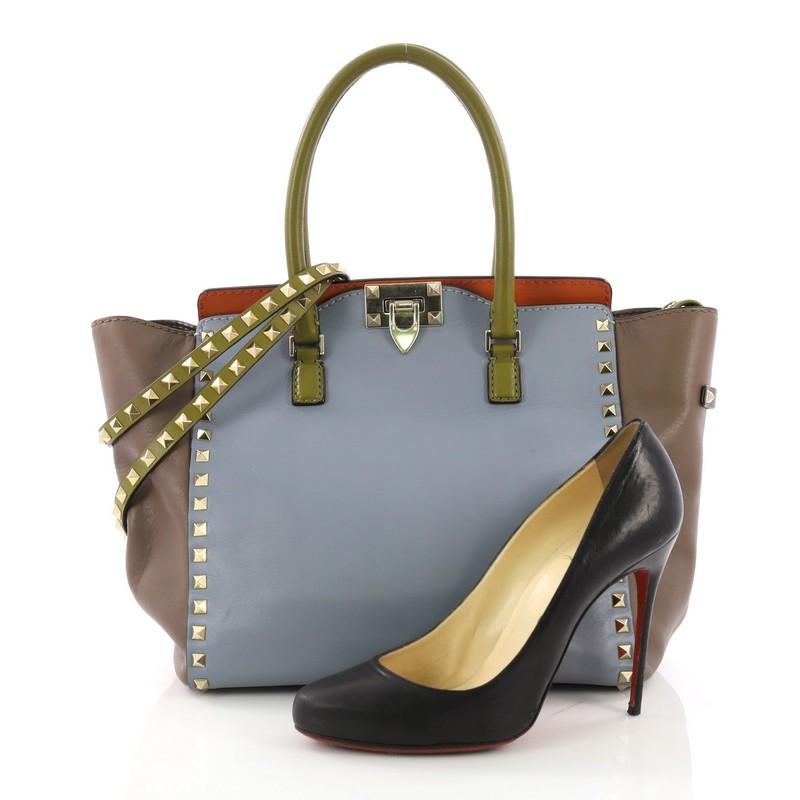 This Valentino Rockstud Tote Rigid Leather Medium, crafted in multicolor rigid leather, features dual rolled handles, pyramid stud borders, and gold-tone hardware. Its flip-clasp and top zip closures open to a beige fabric interior with zip and slip