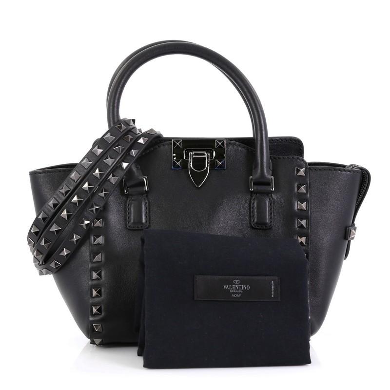 This Valentino Rockstud Tote Rigid Leather Mini, crafted from black rigid leather, features pyramid stud border, dual rolled handles, and gunmetal-tone hardware. Its flip-clasp and top zip closure opens to a black leather interior with zip and slip