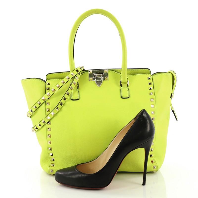 This Valentino Rockstud Tote Rigid Leather Small, crafted in neon green rigid leather, features dual rolled handles, pyramid stud borders, and gold-tone hardware. Its flip-clasp and top zip closures open to a beige fabric interior with zip and slip