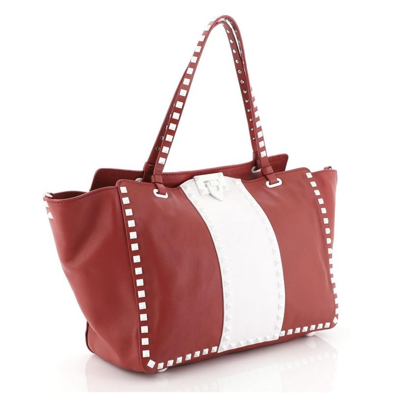 This Valentino Rockstud Tote Soft Leather Medium, crafted from white and red soft leather, features dual tall handles, pyramid stud trim details, and silver-tone hardware. Its clasp lock closure opens to a neutral fabric interior with side zip