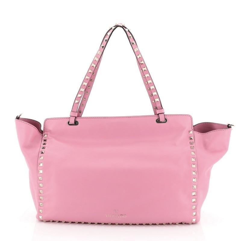 This Valentino Rockstud Tote Soft Leather Medium, crafted from pink soft leather, features dual tall handles, pyramid stud trim details, and gold-tone hardware. Its clasp lock closure opens to a neutral fabric interior with side zip pocket.